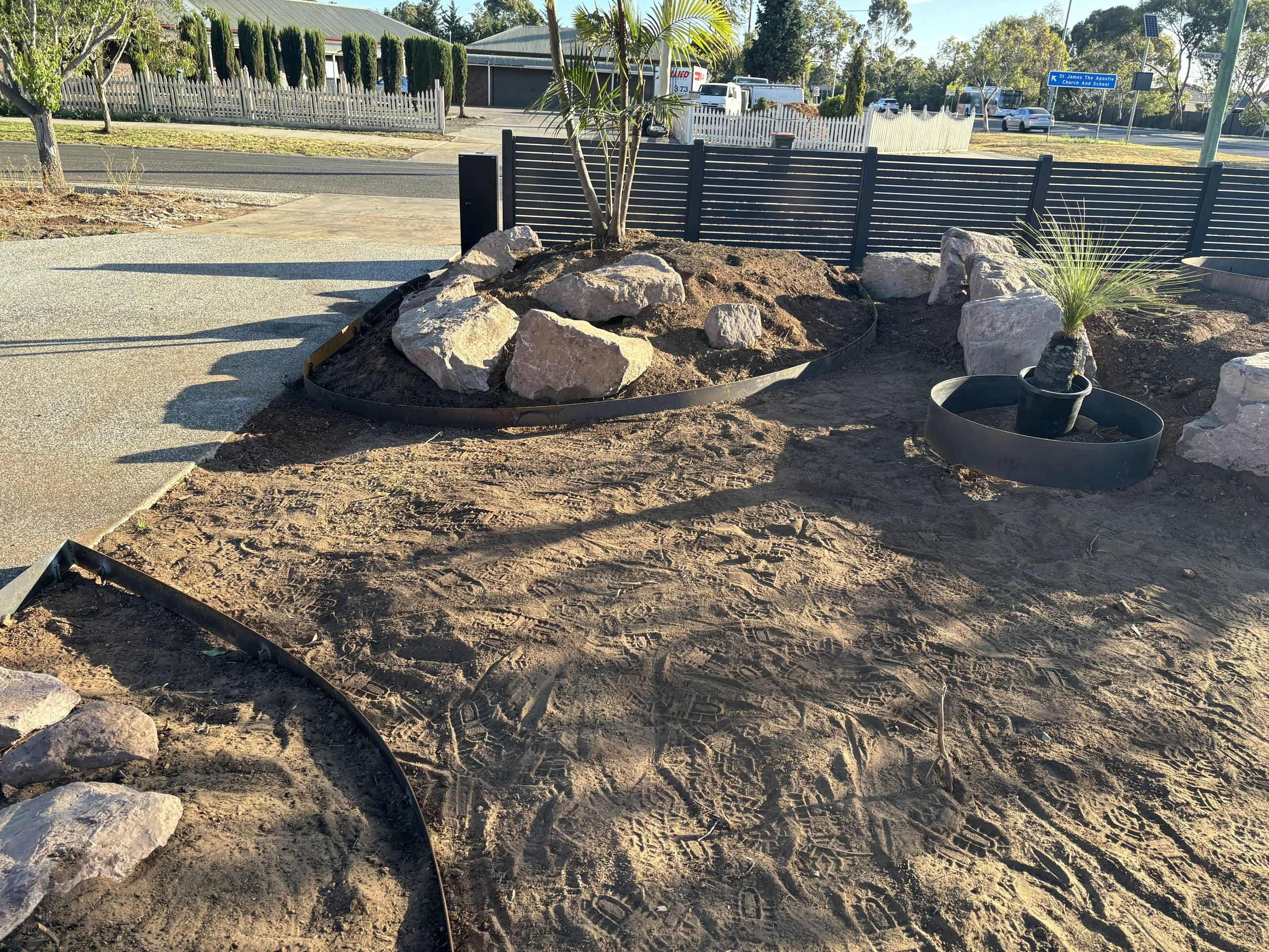 Landscaping in progress with two small areas containing large rocks and a potted palm
