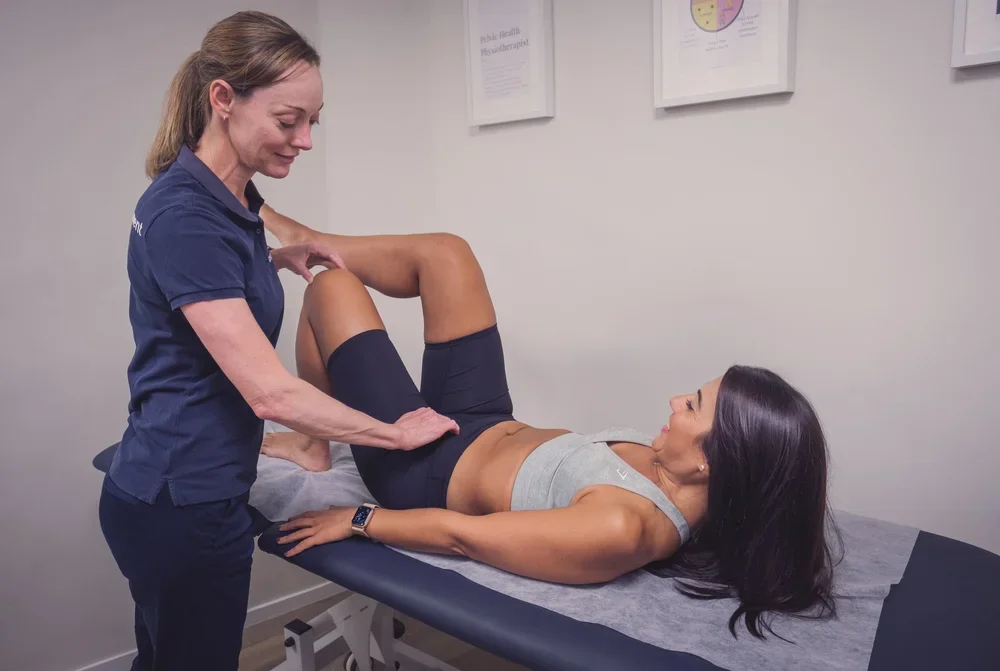 A physical therapist or medical professional performs a knee examination on a woman lying on an exam table.