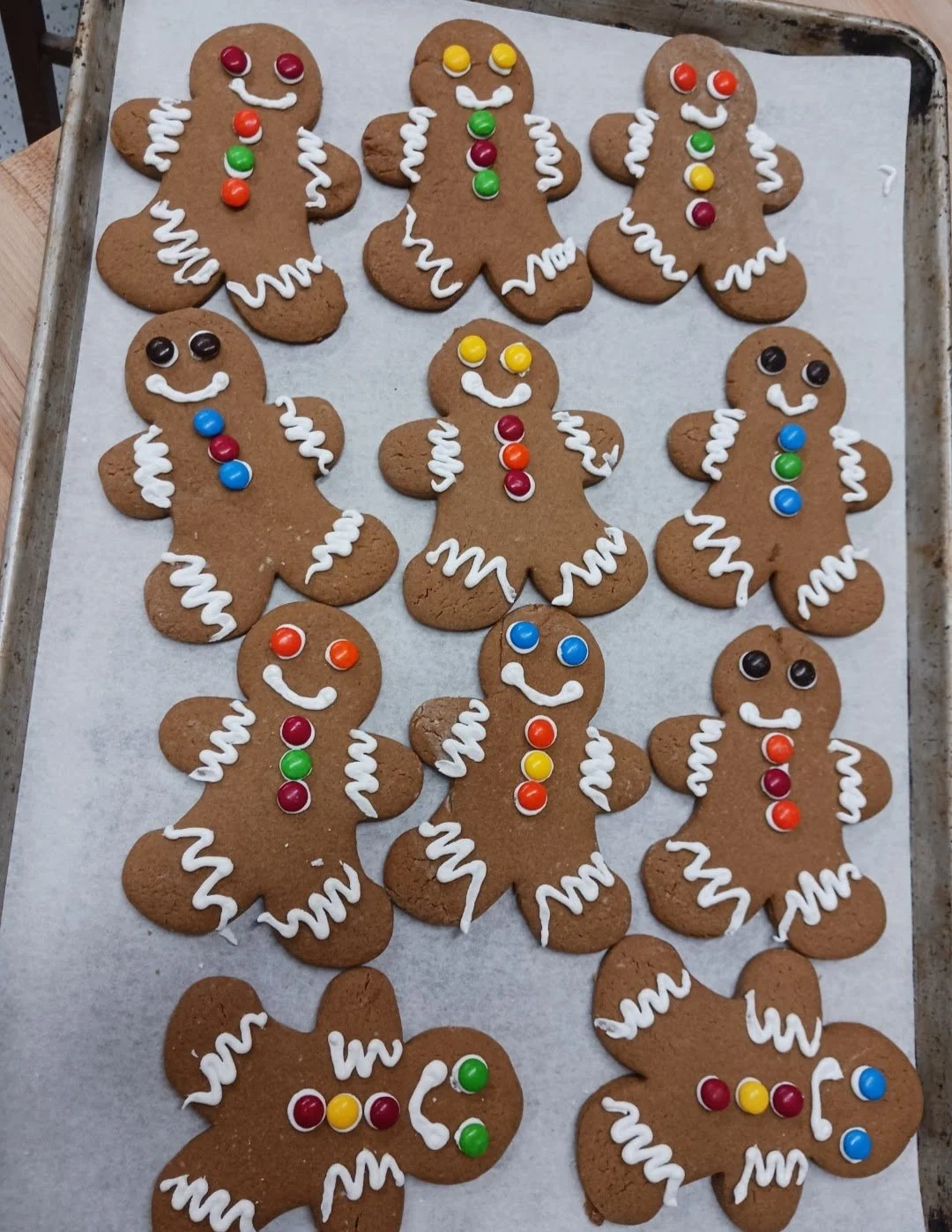A tray of decorated gingerbread cookies shaped like gingerbread men, decorated with white icing, colorful candies for buttons, and eyes.