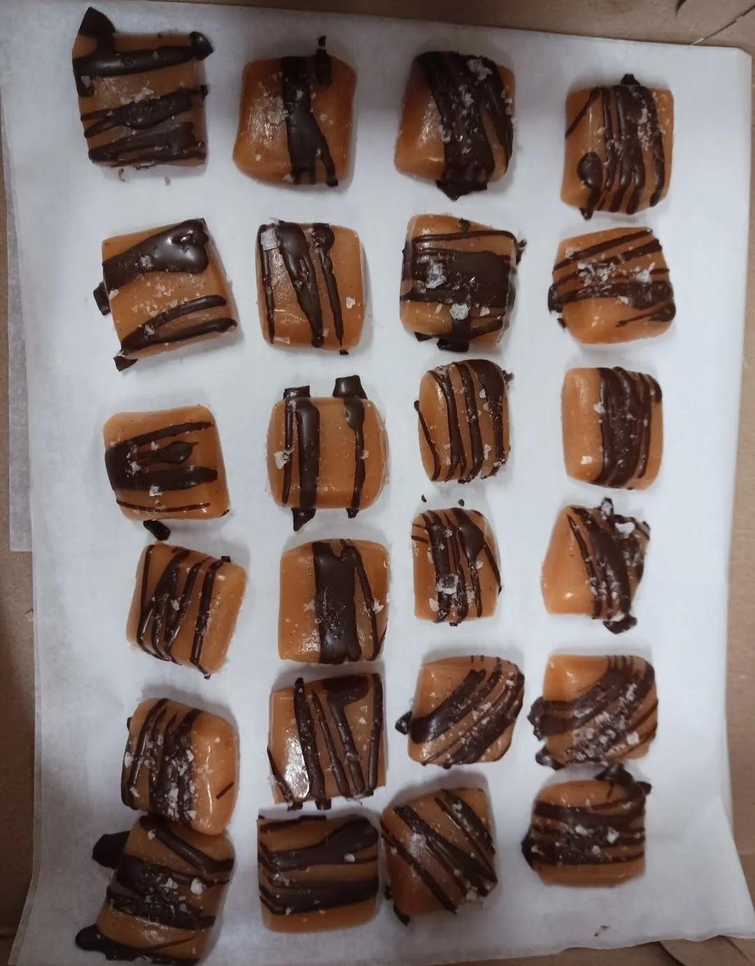 Assorted square caramel candies with chocolate drizzle on parchment paper.