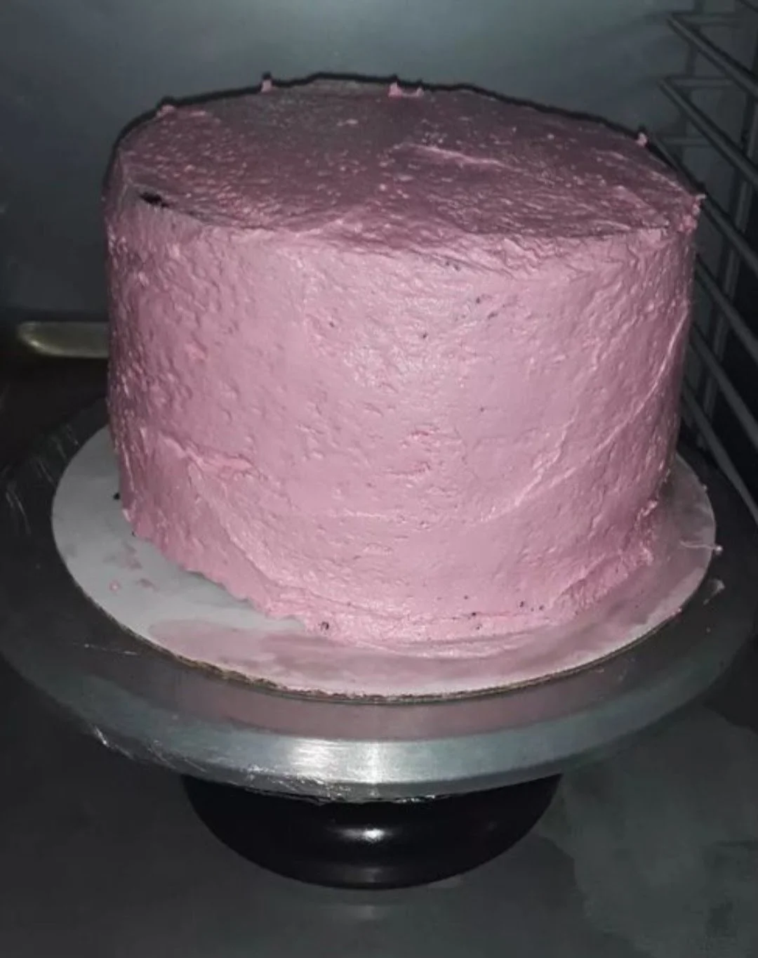 Pink frosted cake on a silver cake turntable.
