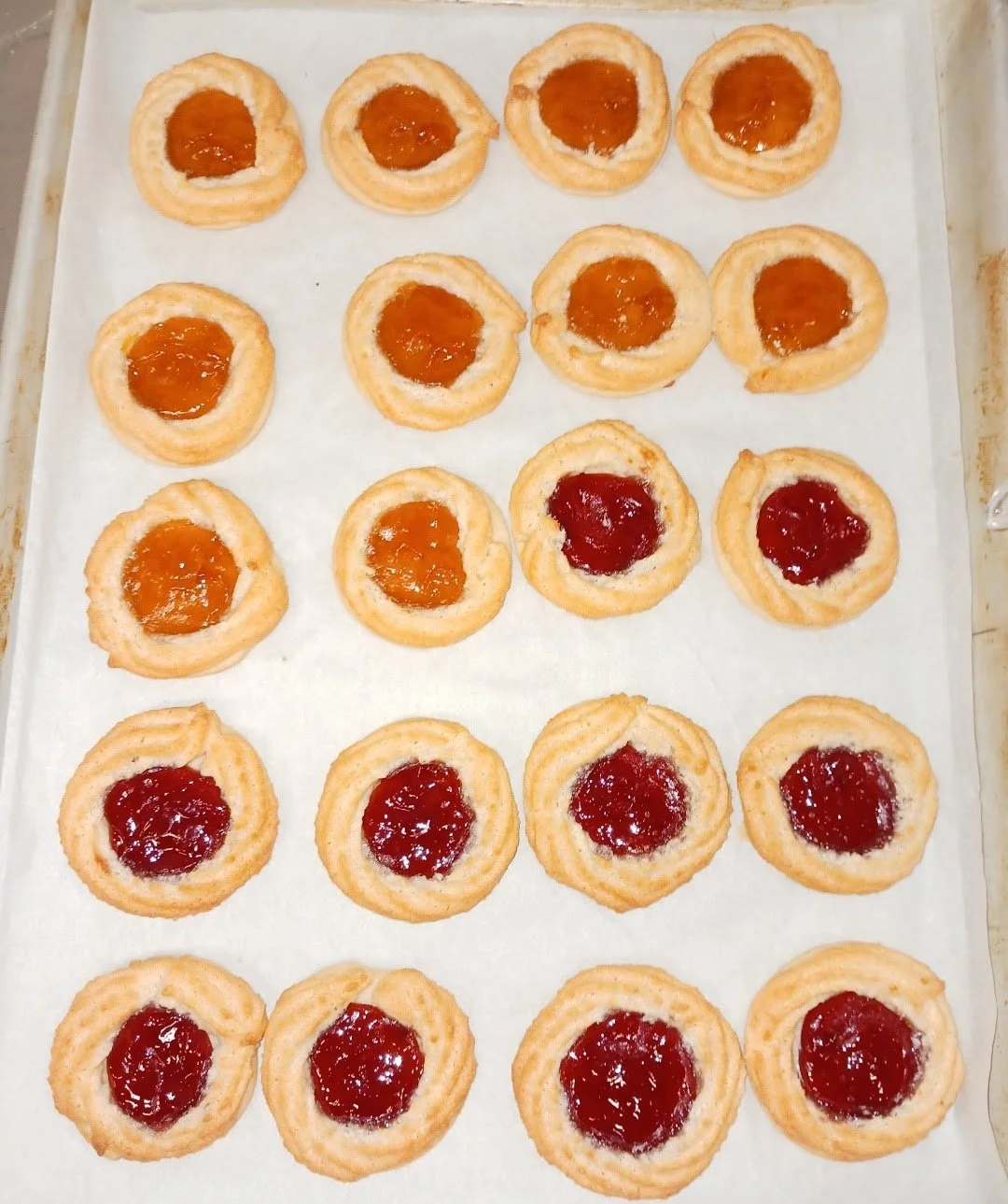 Assorted fruit tarts with different fruit jams on a baking sheet.