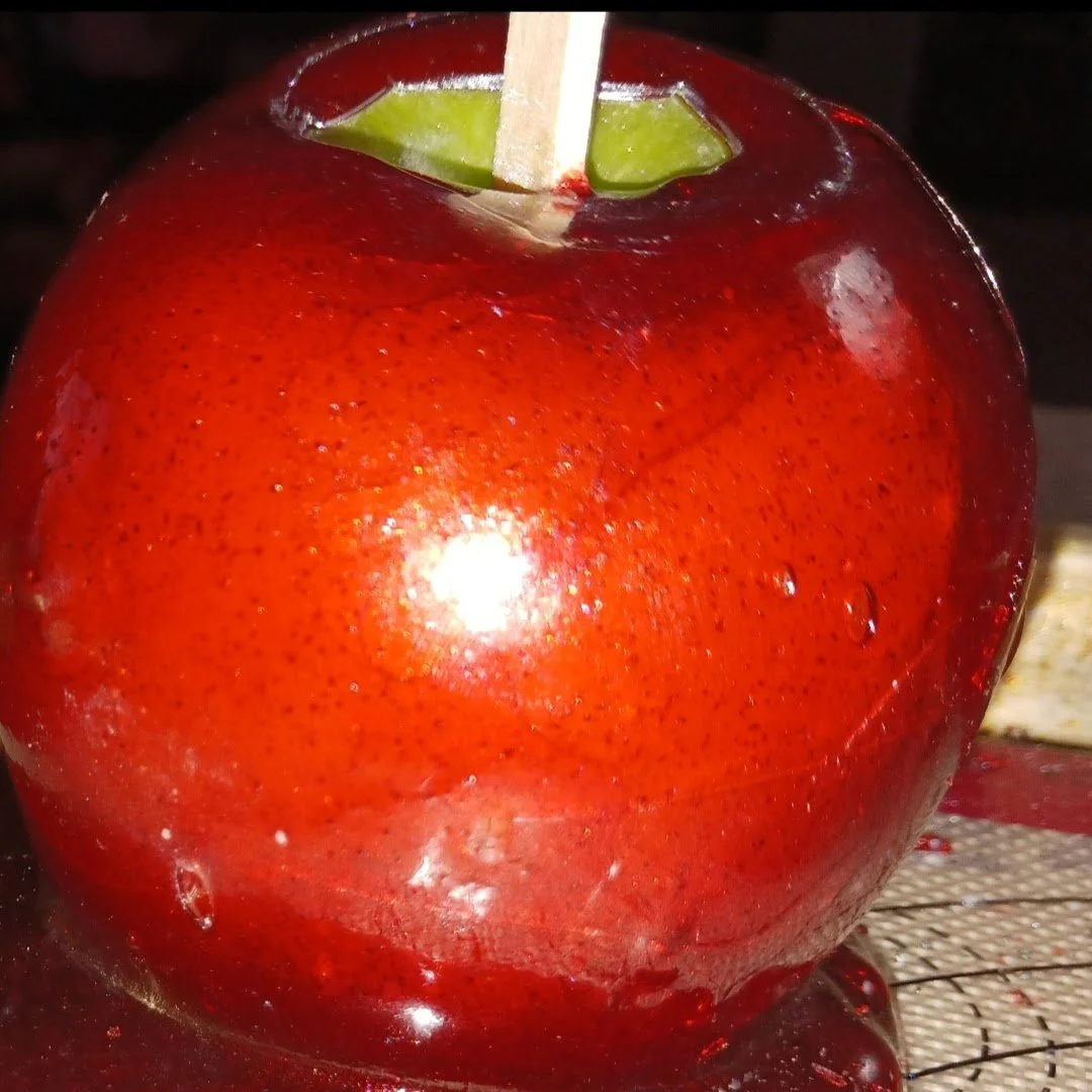 Close-up of a red candied apple with a green apple inside, placed on a cooling rack.