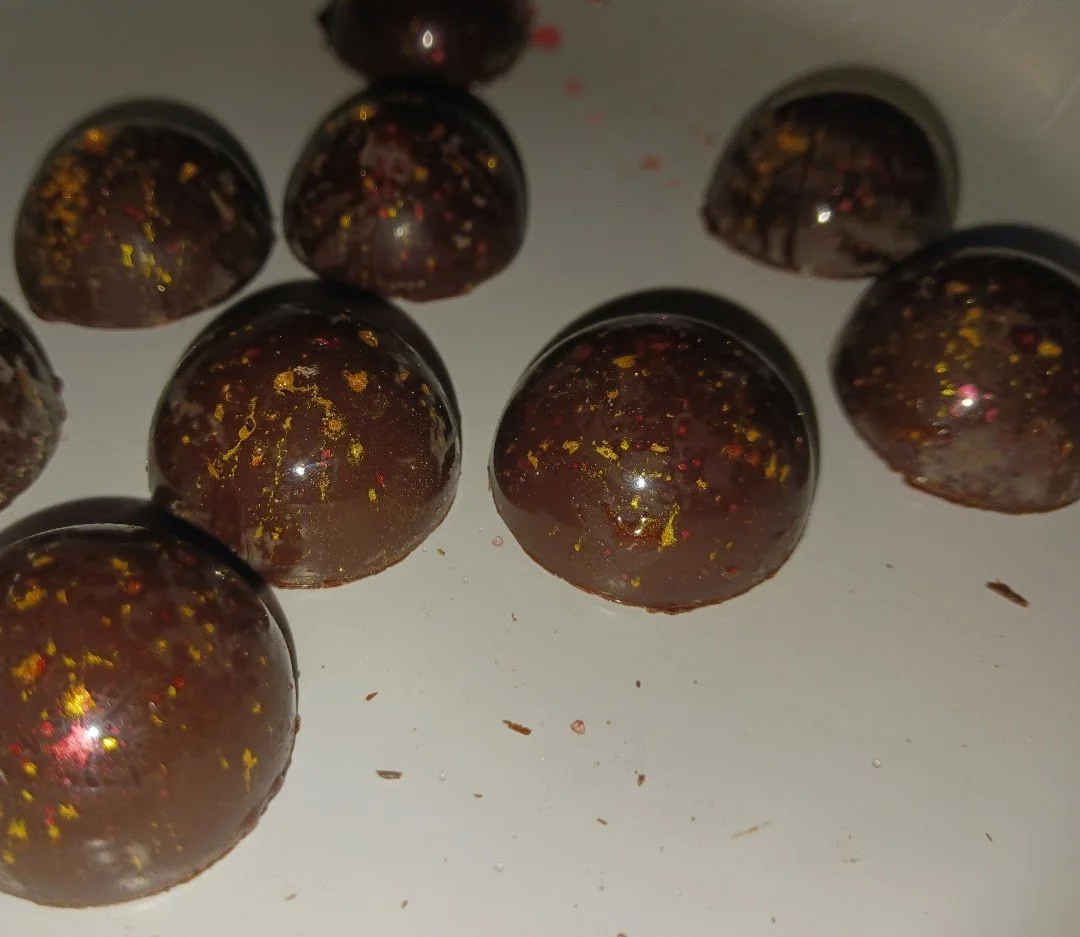 Close-up of dark chocolate truffles with gold flecks on a white surface.