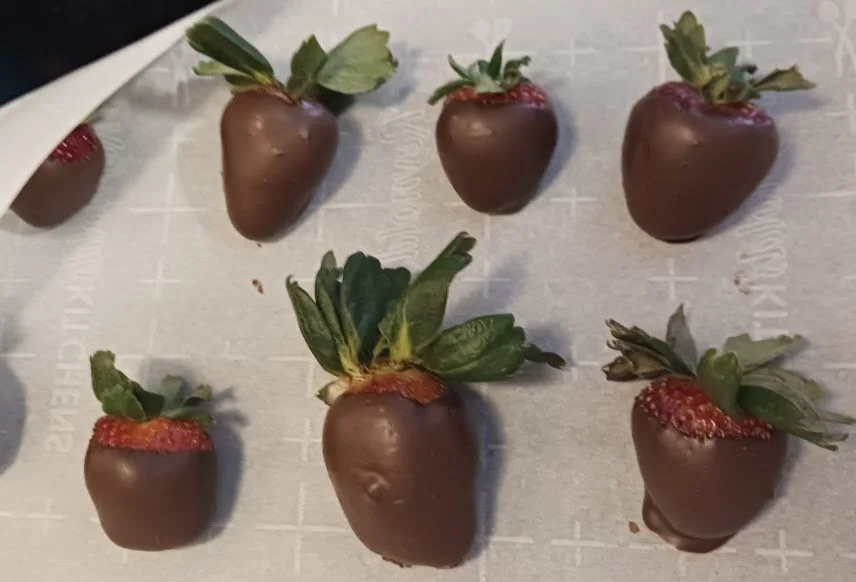 Strawberries partially dipped in chocolate, placed on a white surface.