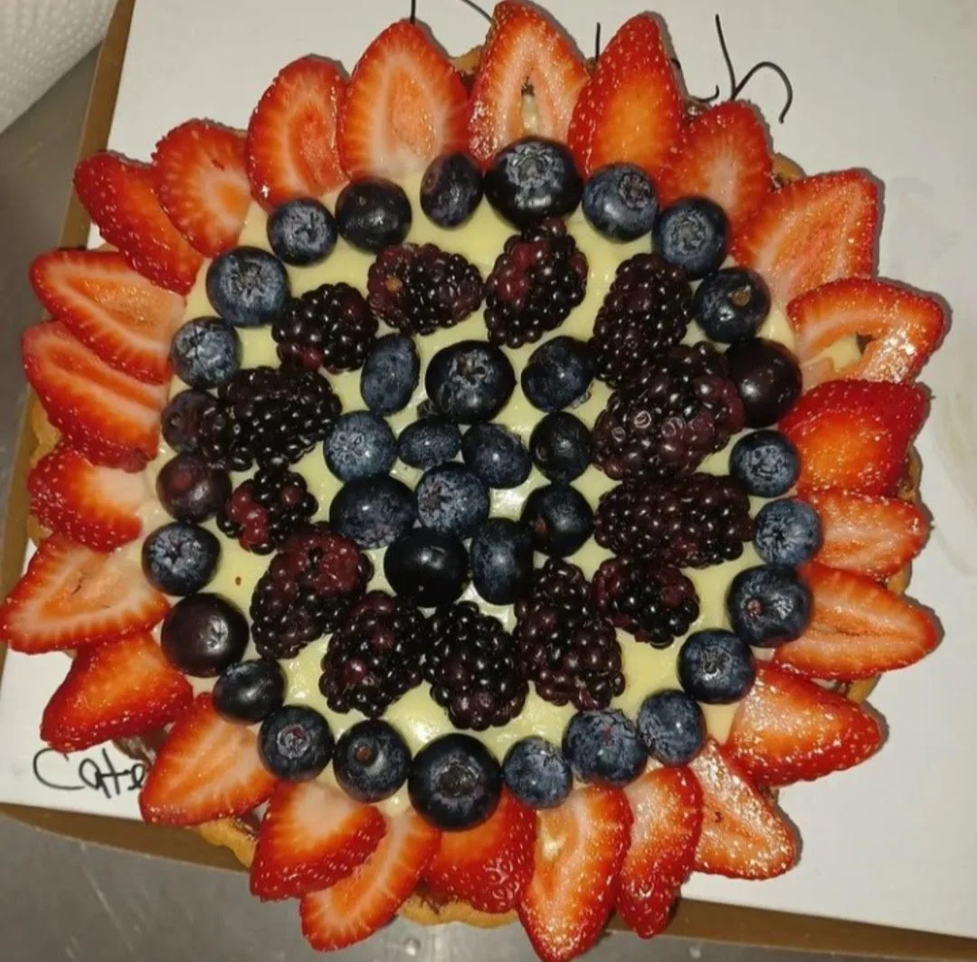 A round fruit tart topped with sliced strawberries around the edge, blueberries, blackberries, and grapes in the center.