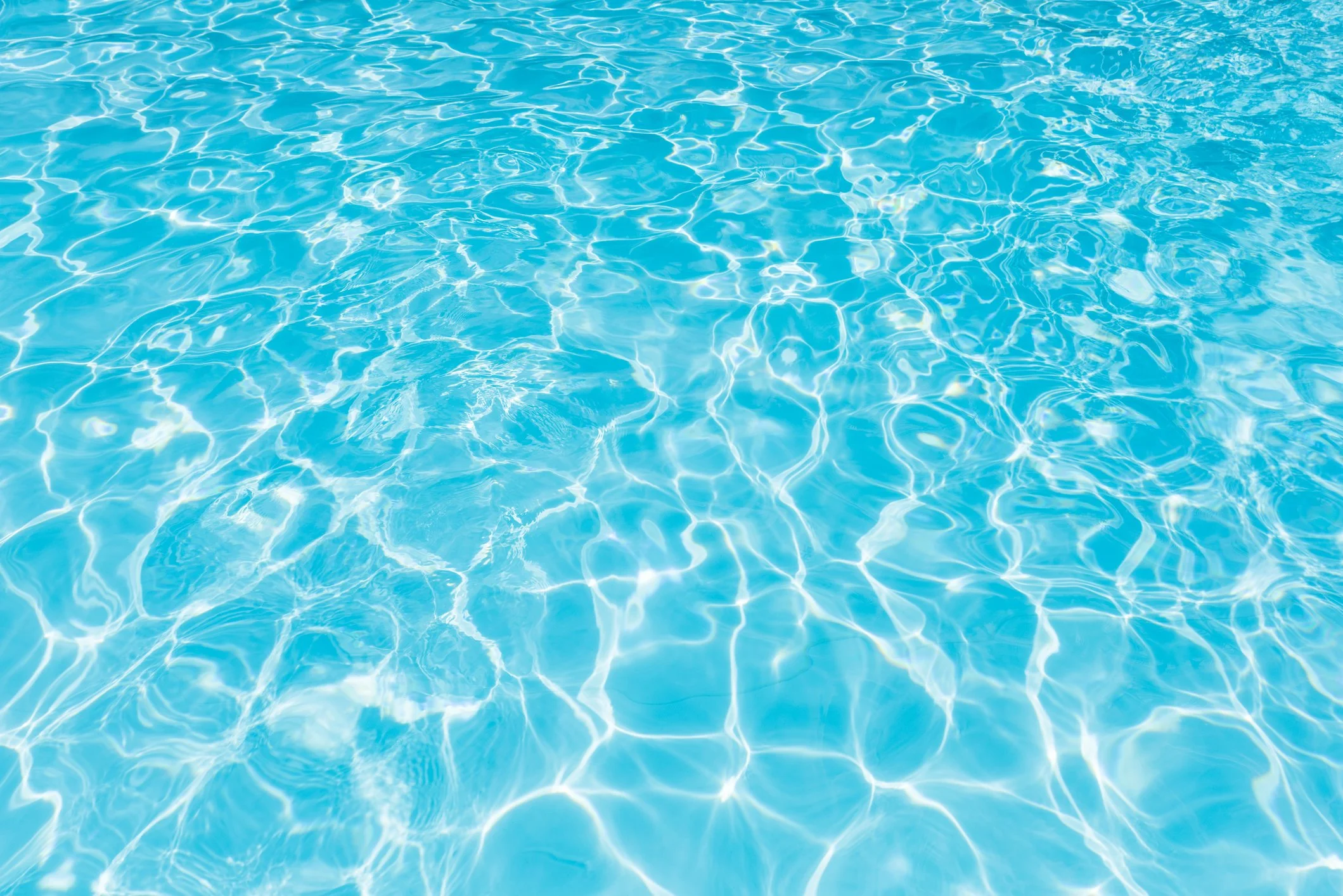 Clear blue swimming pool water showing shimmering reflections and gentle ripples.
