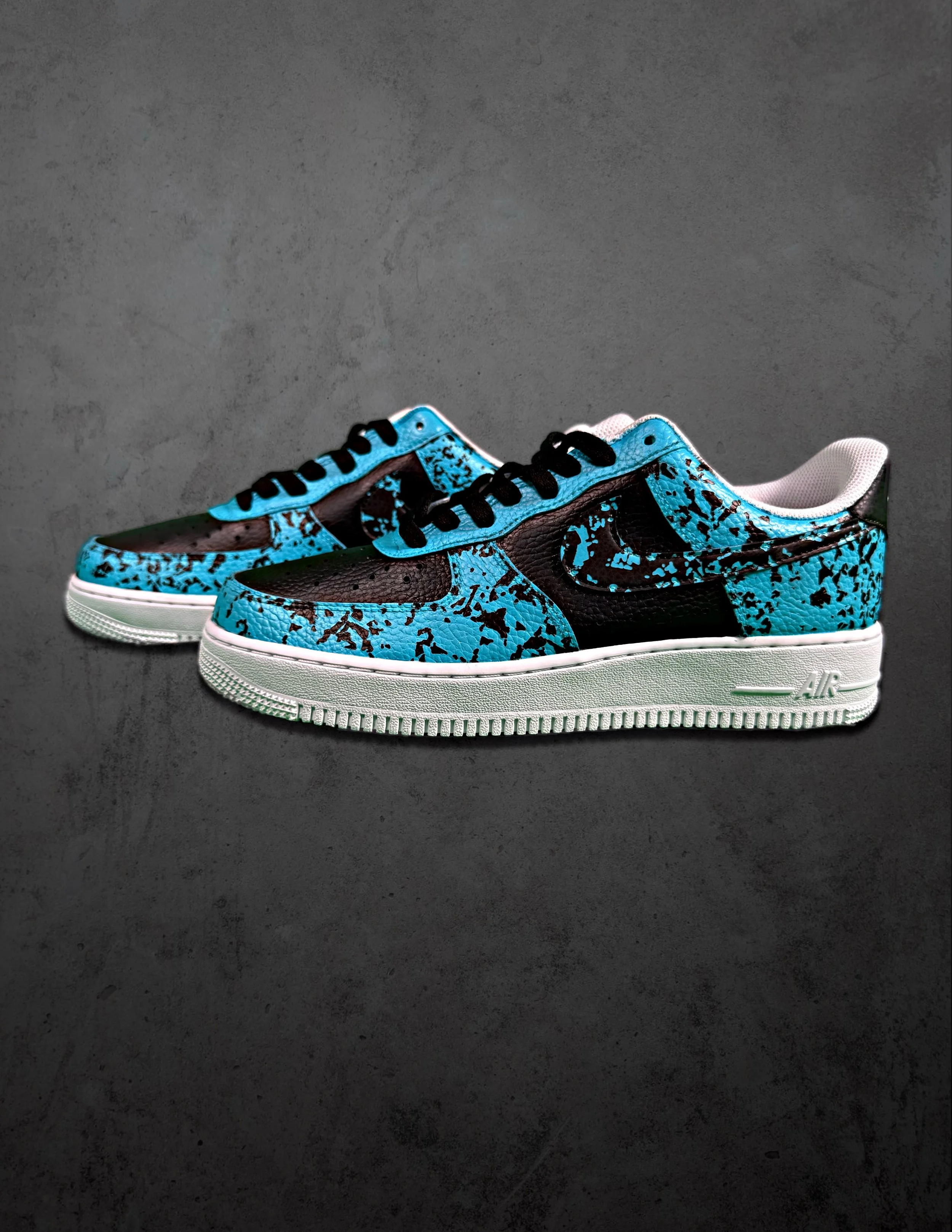 Pair of Nike Air sneakers with a blue, black, and brown splattered pattern on a dark textured surface.