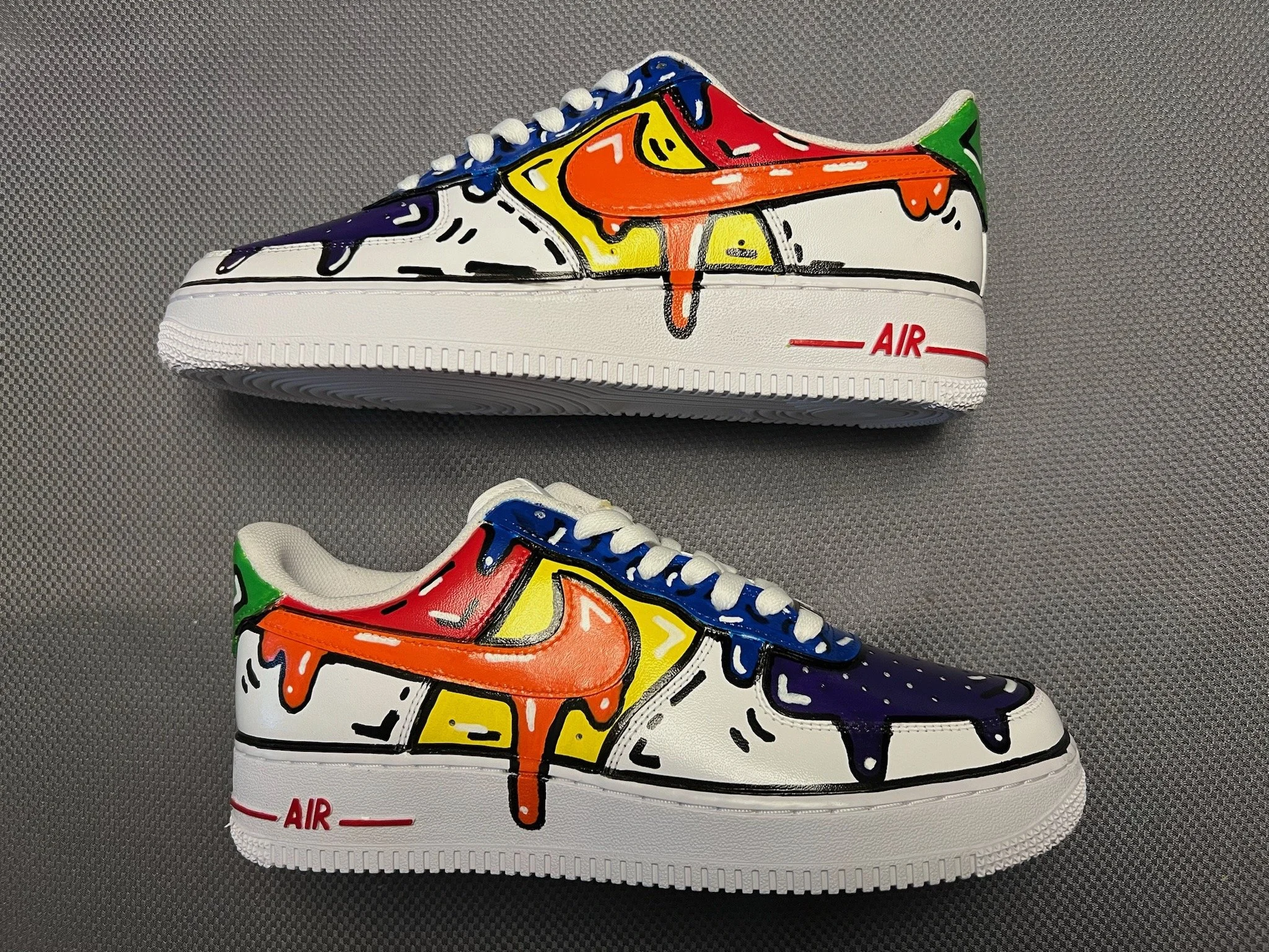 Pair of white Nike Air Force 1 sneakers decorated with colorful graffiti-style paint splatters and outlines, featuring orange, yellow, purple, green, and black accents.