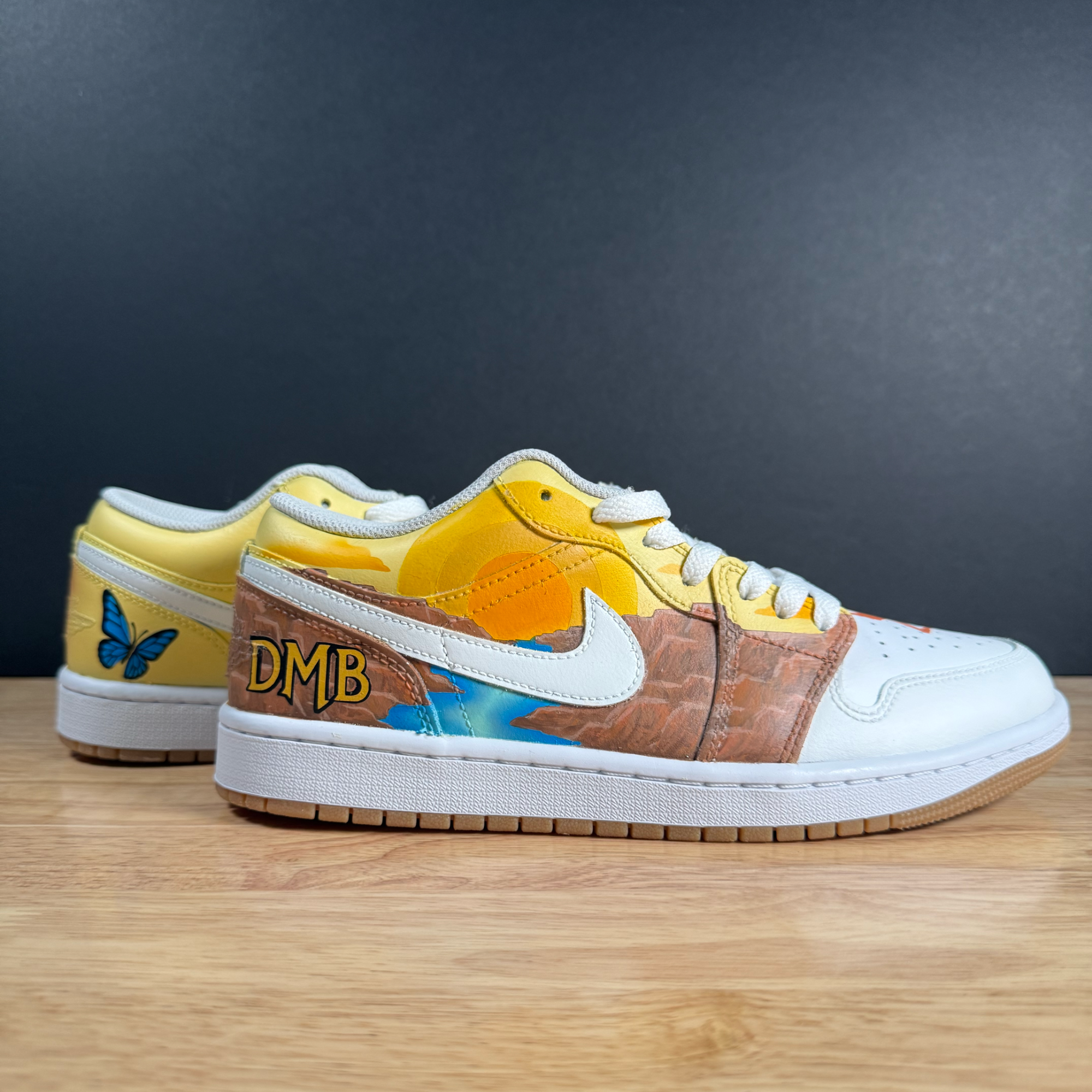 Part of a colorful sneaker with yellow, white, and orange accents and a butterfly design, placed on a wooden surface."}
