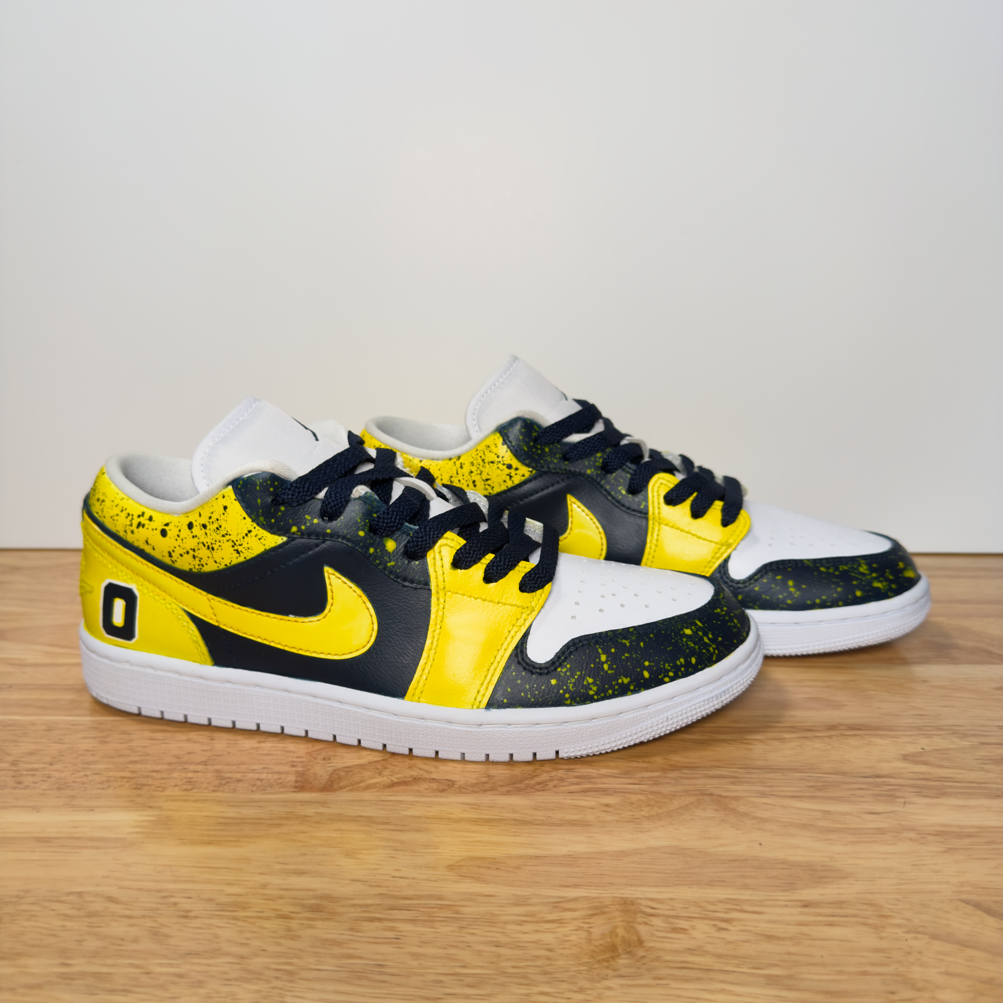 Colorful sneakers featuring black, yellow, and white with black laces, placed on a wooden floor against a plain white background.