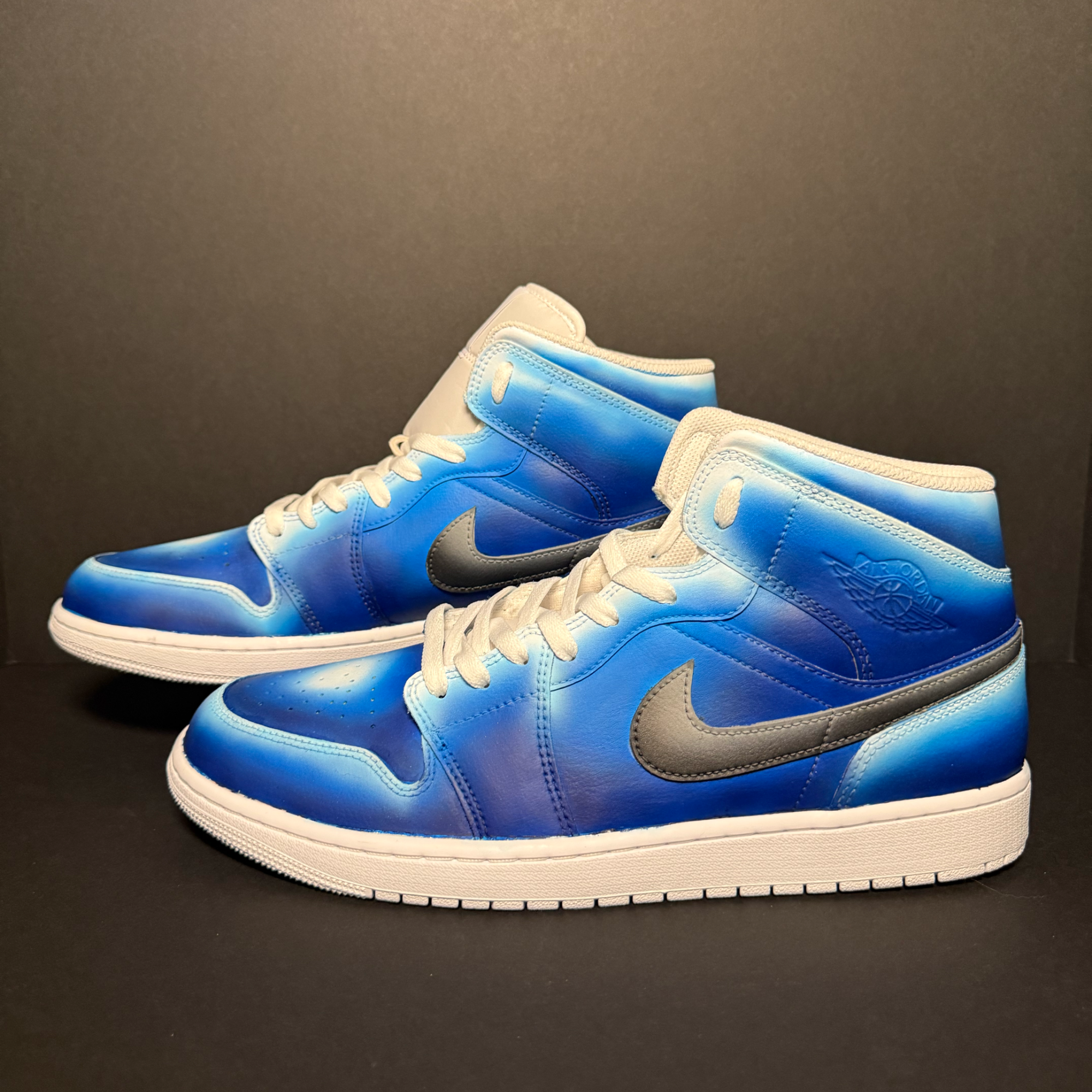 Close-up of a pair of blue and white sneakers on a black surface with a dark background.