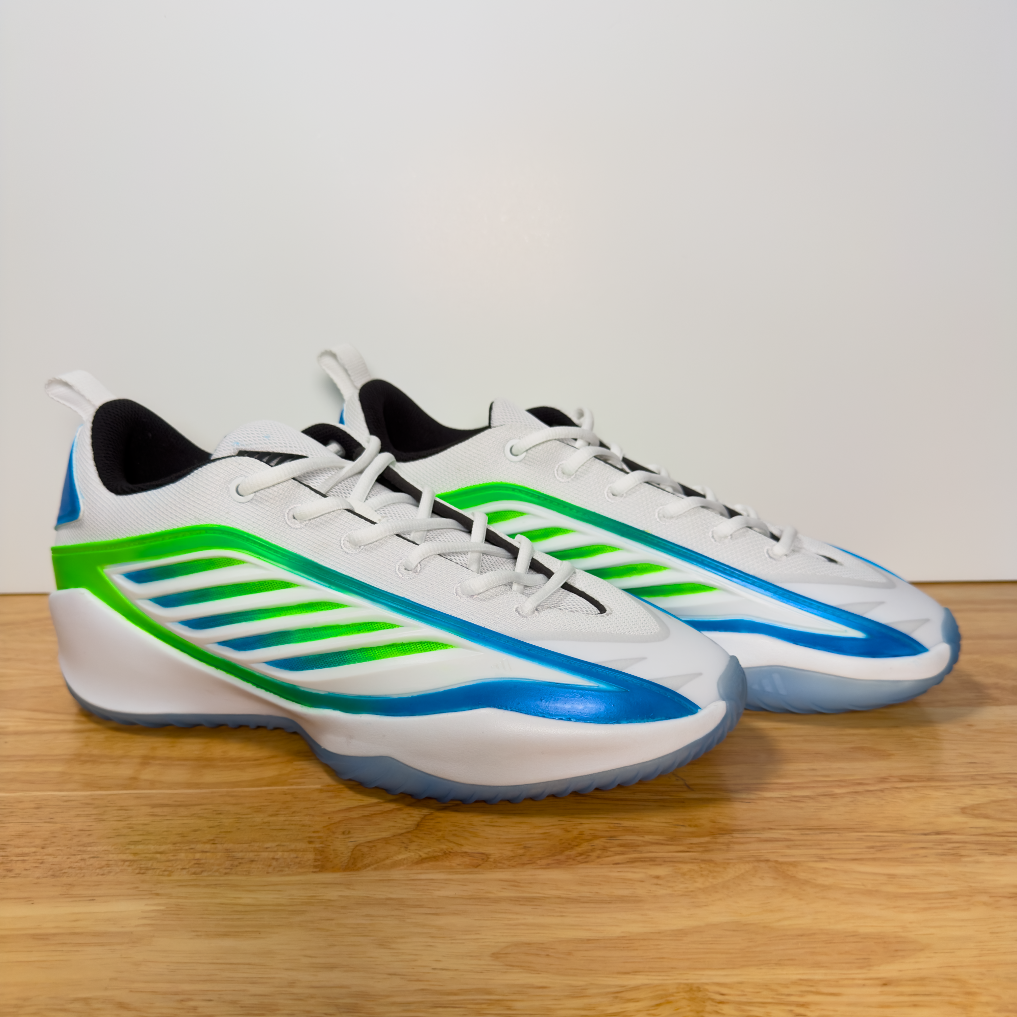 A pair of white athletic shoes with blue and green accents, viewed from above on a wooden surface.