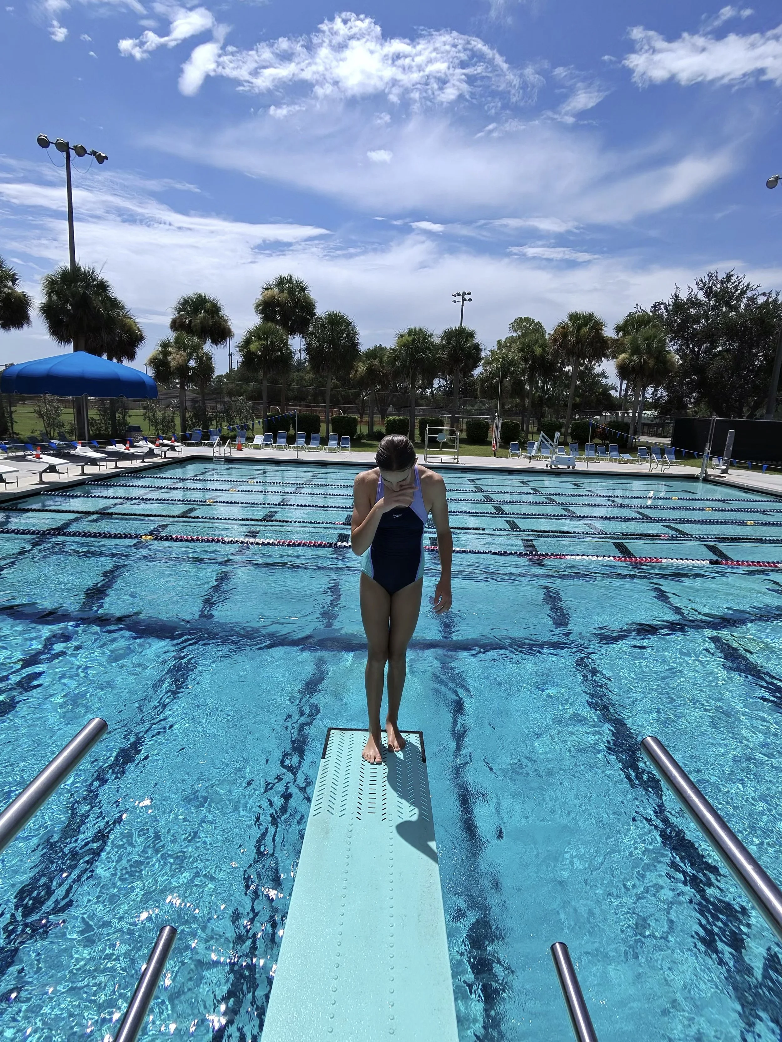 A female Pelican Diving Team member is standing on the end of the 1-meter diving board at Golden Gate Aquatic Facility.