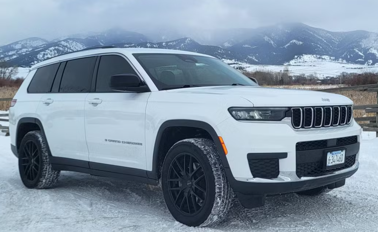 White Jeep Grand Cherokee parked on snow-covered ground with snow-capped mountains in the background.
