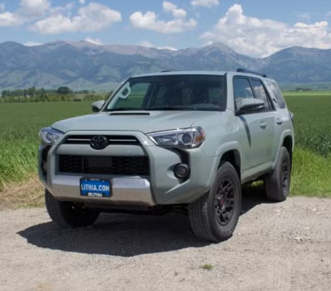 Gray Toyota SUV parked on a dirt road with green fields and mountains in the background.
