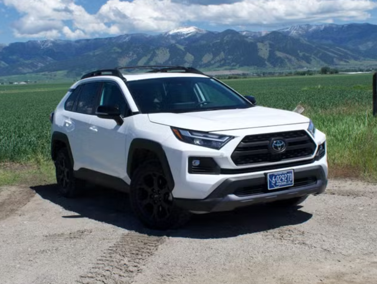 White SUV parked on a dirt road with mountains and blue sky in the background.