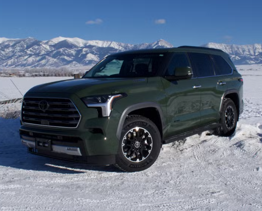 Green SUV parked on snowy ground with snow-covered mountains in the background.