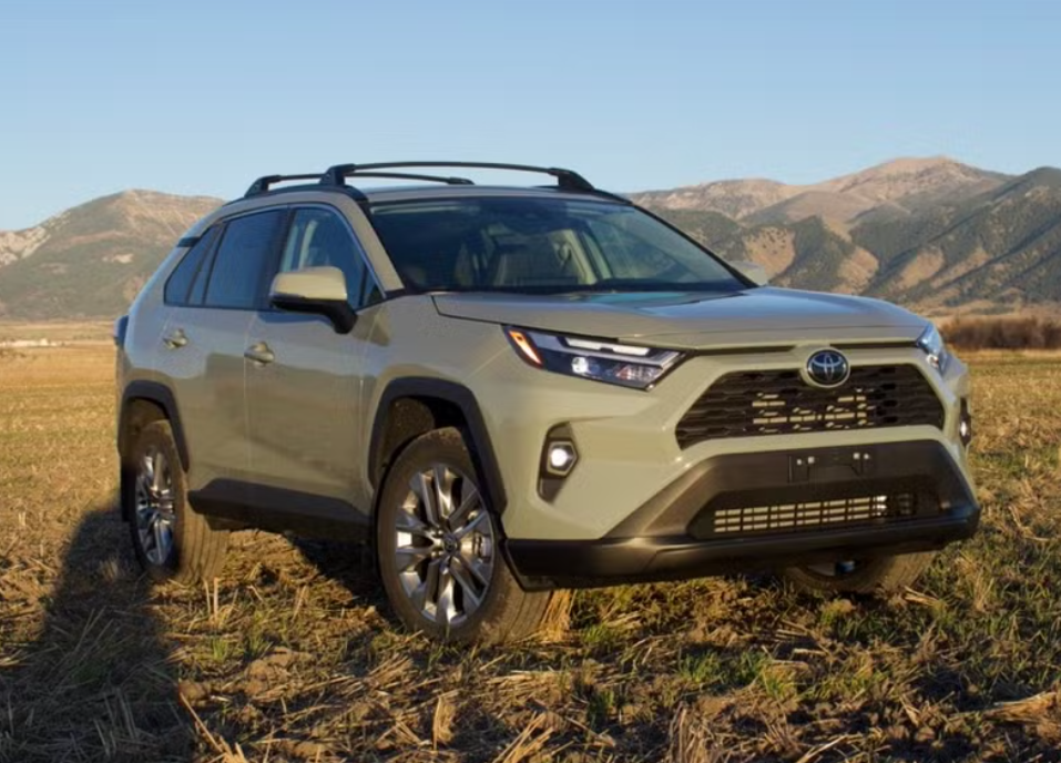 A beige Toyota RAV4 SUV parked on a field with mountains in the background under a clear sky.