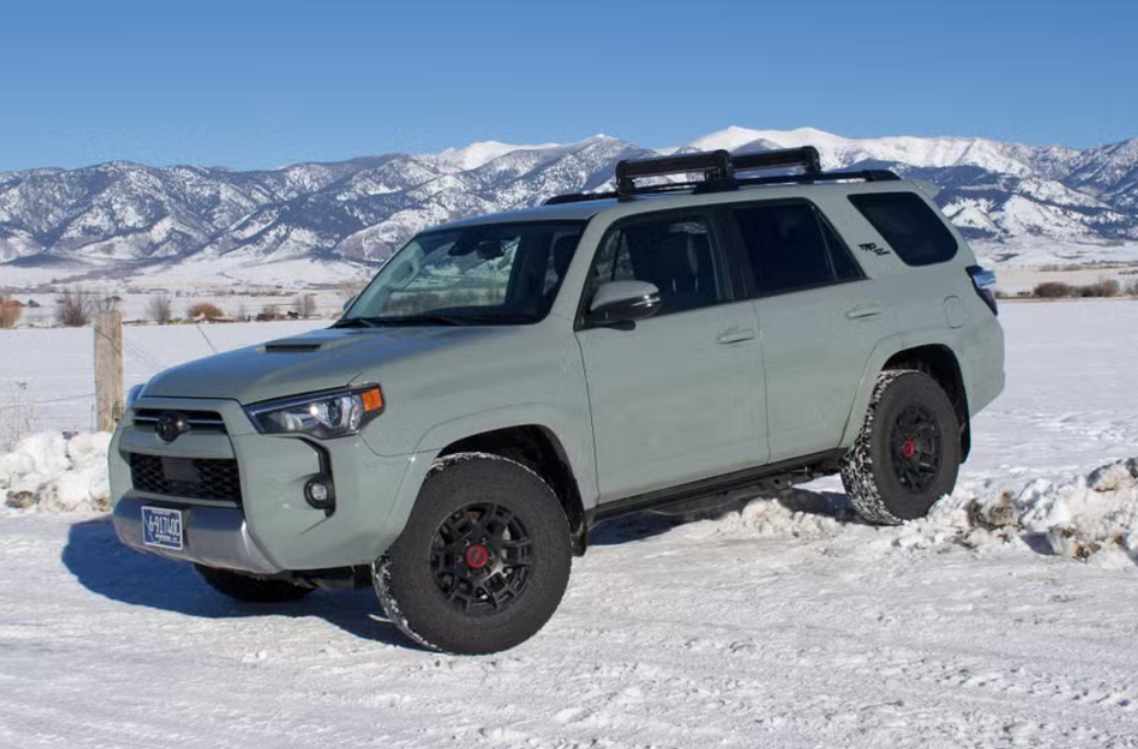 A light green Toyota SUV parked on snow-covered ground with snow-capped mountains in the background.