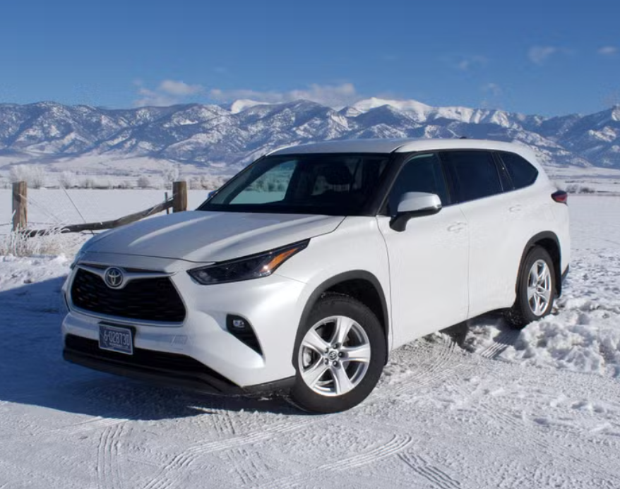White Toyota SUV parked on snowy ground with snow-capped mountains in the background on a clear, sunny day.