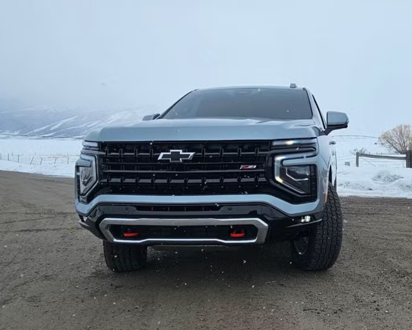 Front view of a gray Chevrolet pickup truck parked on a dirt road near snow-covered fields and hills.