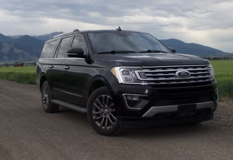 A black Ford SUV parked on a dirt road with green fields and mountains in the background.