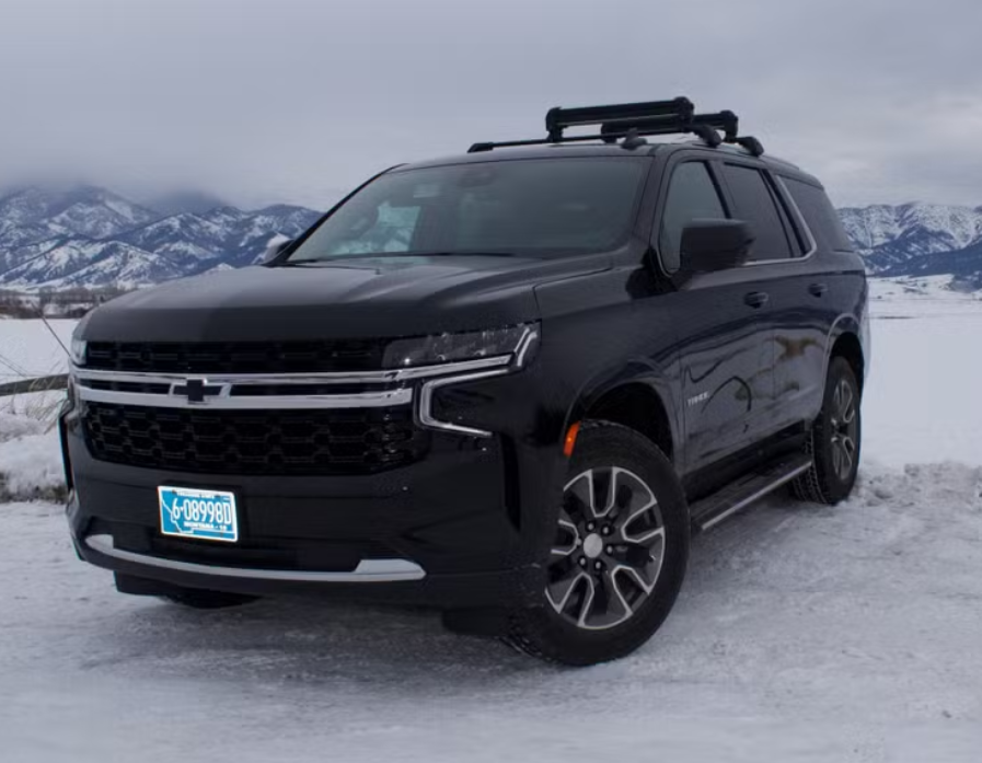 Black Chevrolet SUV parked on snowy terrain with mountains in the background.