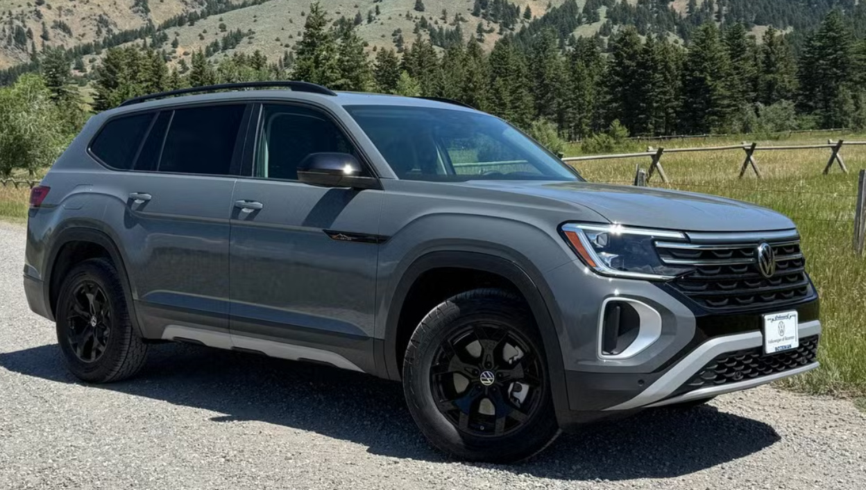 Gray Volkswagen SUV parked on a gravel road with trees and mountains in the background.