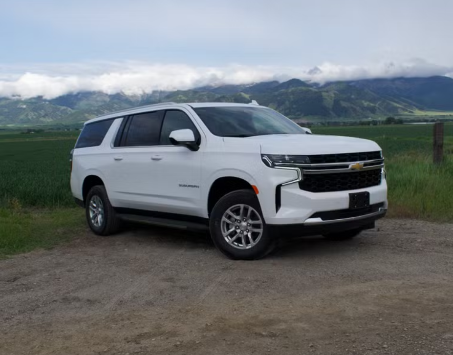 White Chevrolet SUV parked on a dirt road with green fields and mountains in the background.