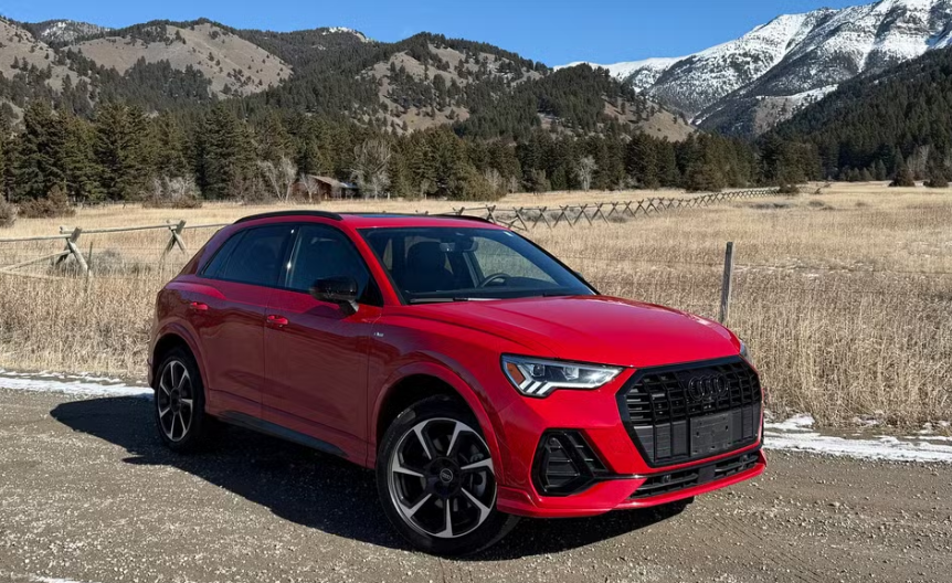 An red Audi SUV parked on a mountain road with trees in the background