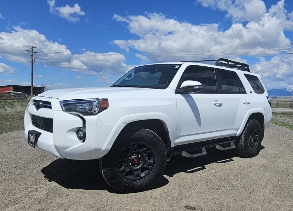 A white SUV parked on a dirt road under a partly cloudy sky.