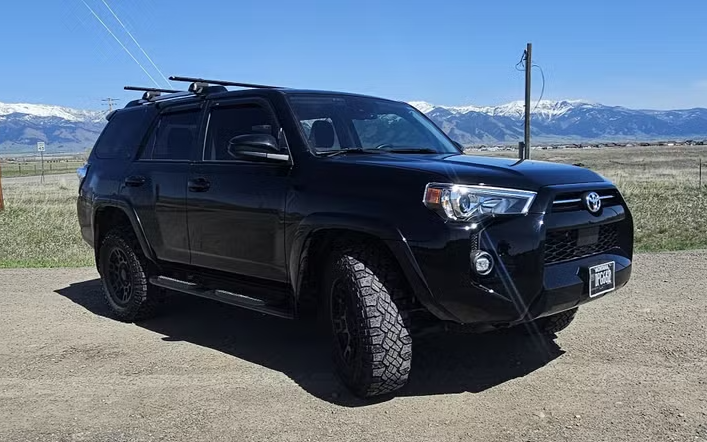 Black Toyota 4Runner SUV parked on a dirt road with mountains in the background.