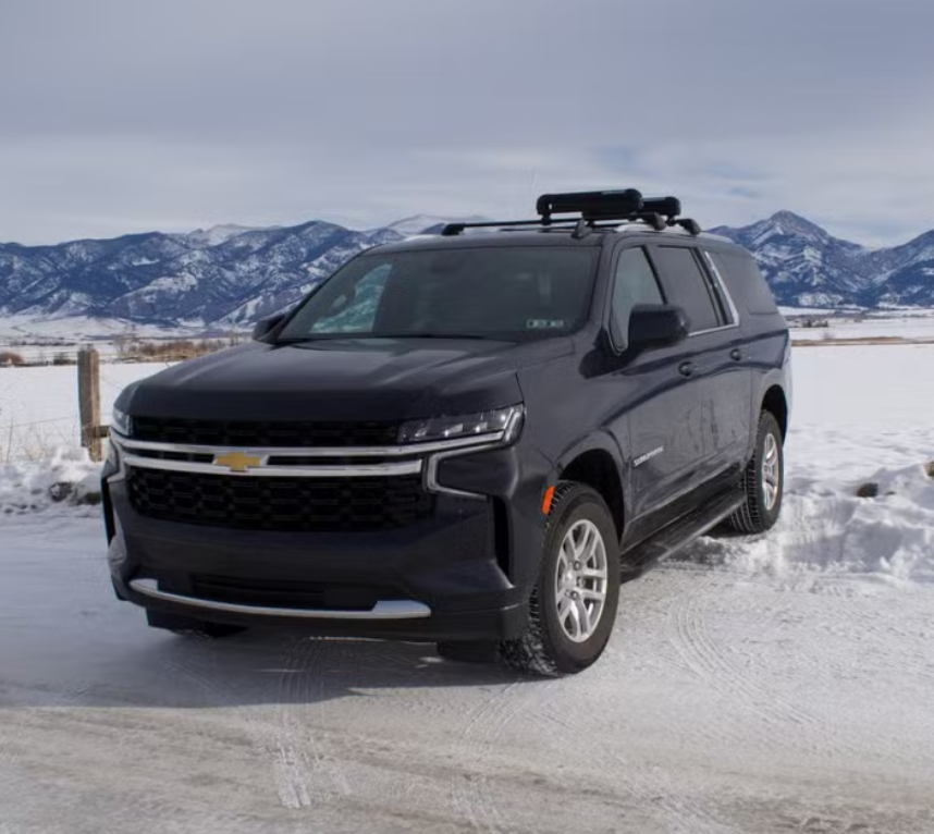 Black Chevrolet SUV parked on snowy road with mountains in the background