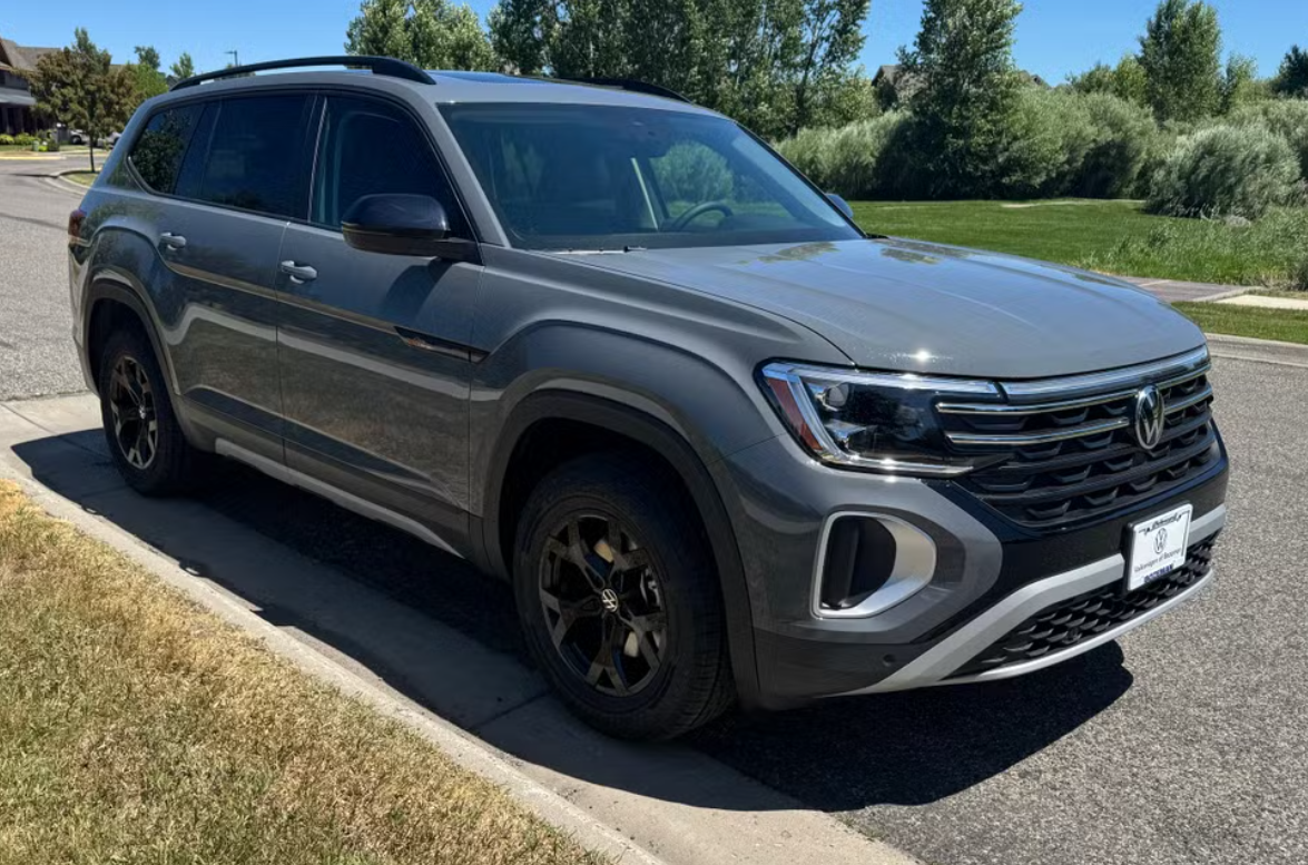 Gray Volkswagen SUV parked on a curb in a suburban area with green grass and trees in the background.