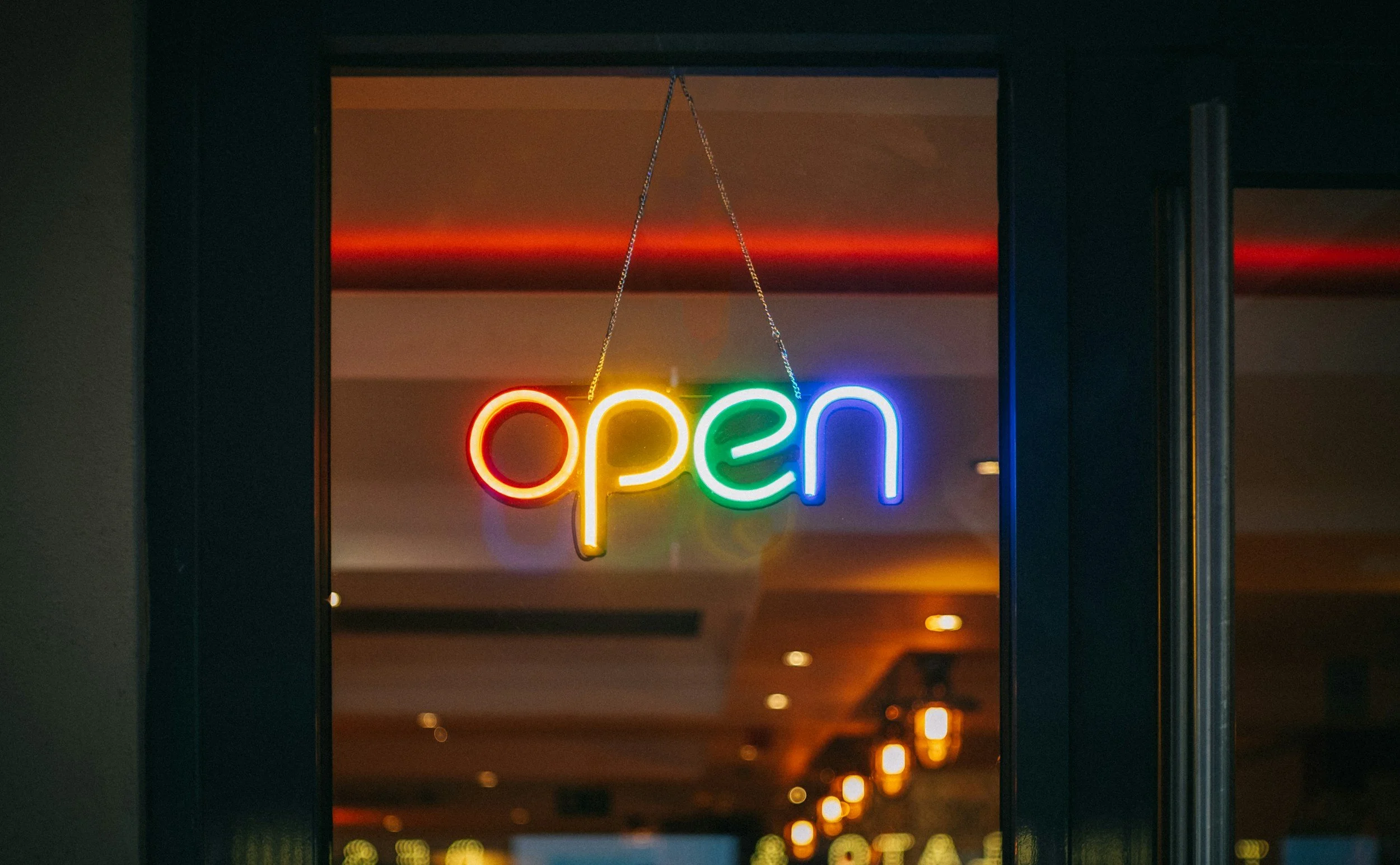 Neon sign saying 'open' hanging inside a building, with warm interior lighting.