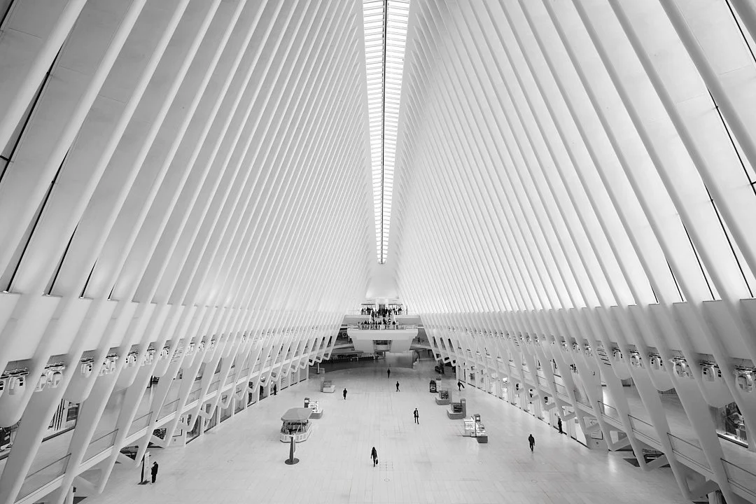 Modern airport terminal with high vaulted ceiling, white structural beams, and people walking inside.