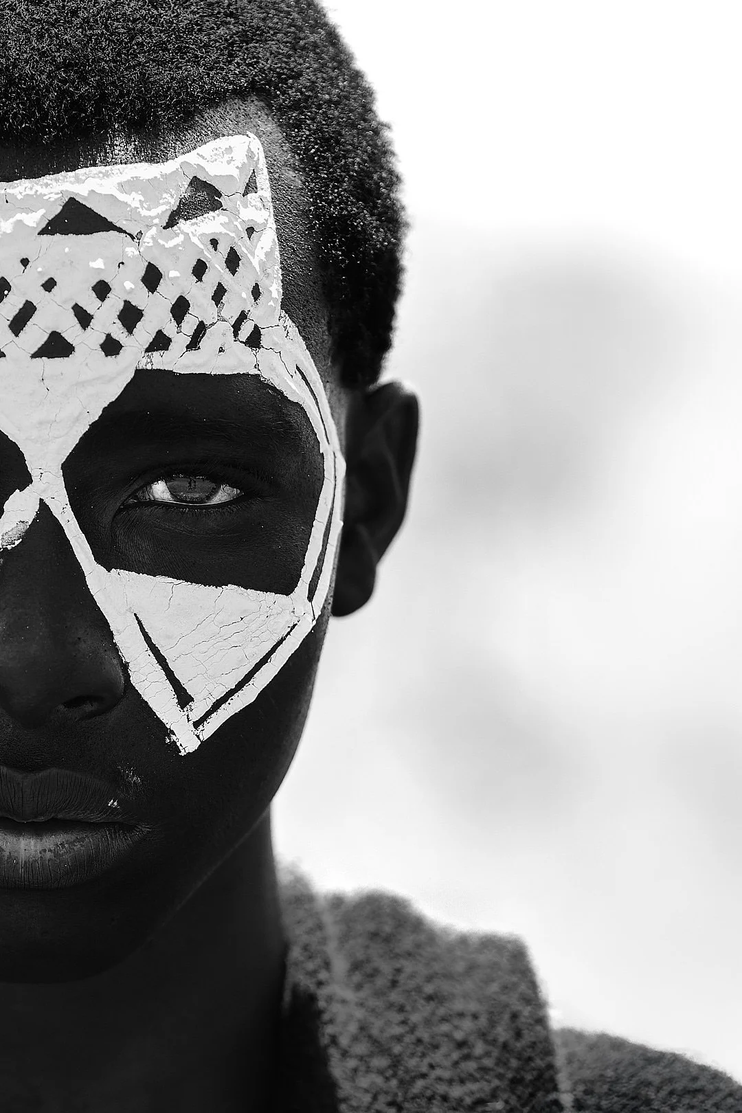 Close-up black and white photo of a person with face paint resembling a skull, highlighting one eye.