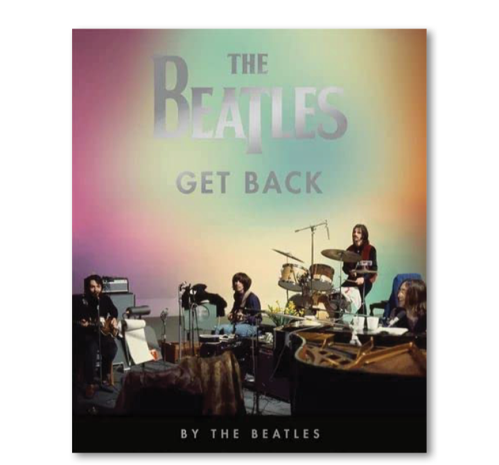 Photo of The Beatles performing on stage with a colorful projected background that reads 'The Beatles Get Back.'