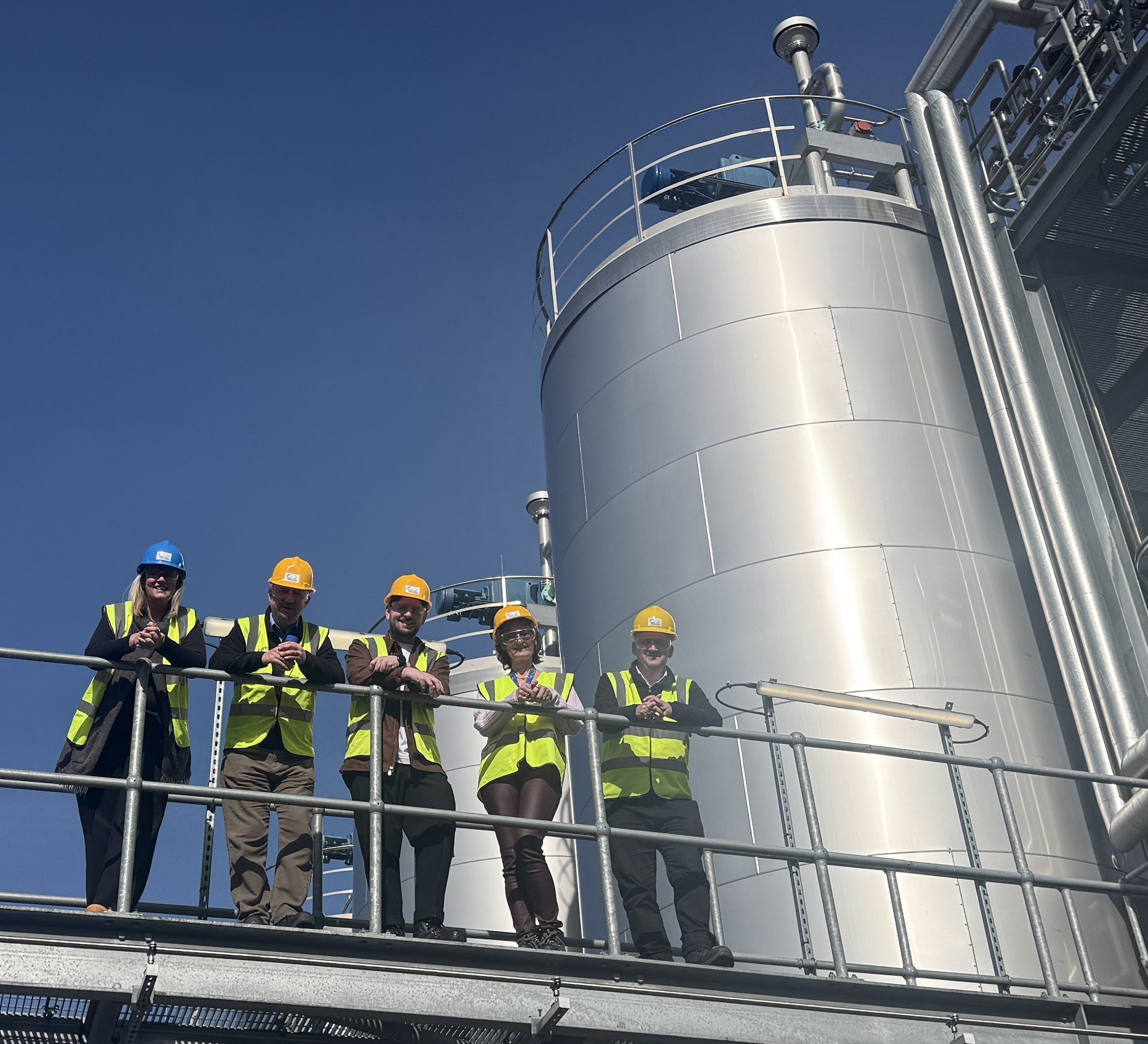 Staff from Celtic Renewables and NCIMB stand on a gantry at the biorefinery, wearing hard hats and hi-vis vests.