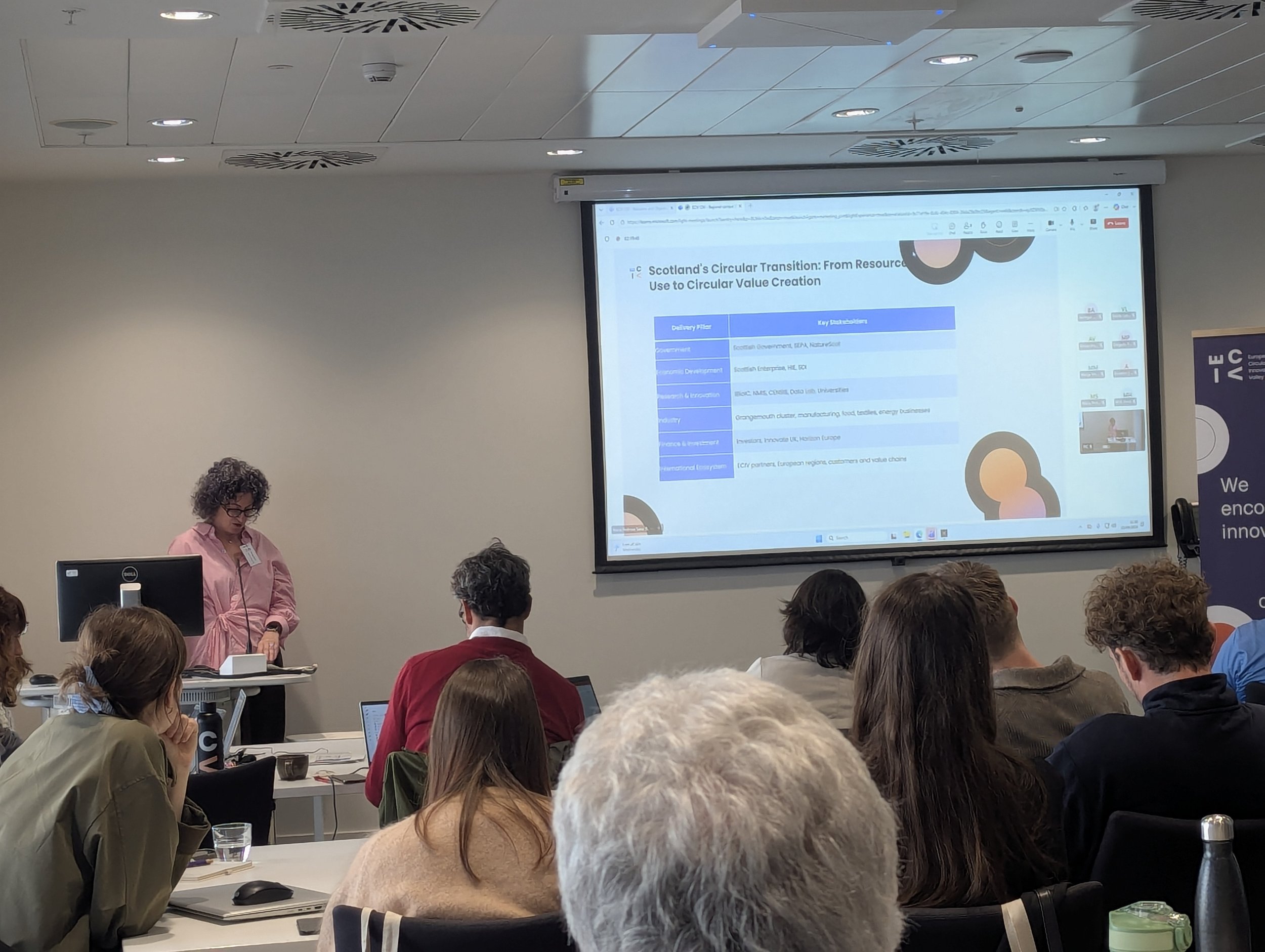 Morag Clark from Scottish Enterprise stands at the front of the room with a screen behind her and ECIV members seated to listen