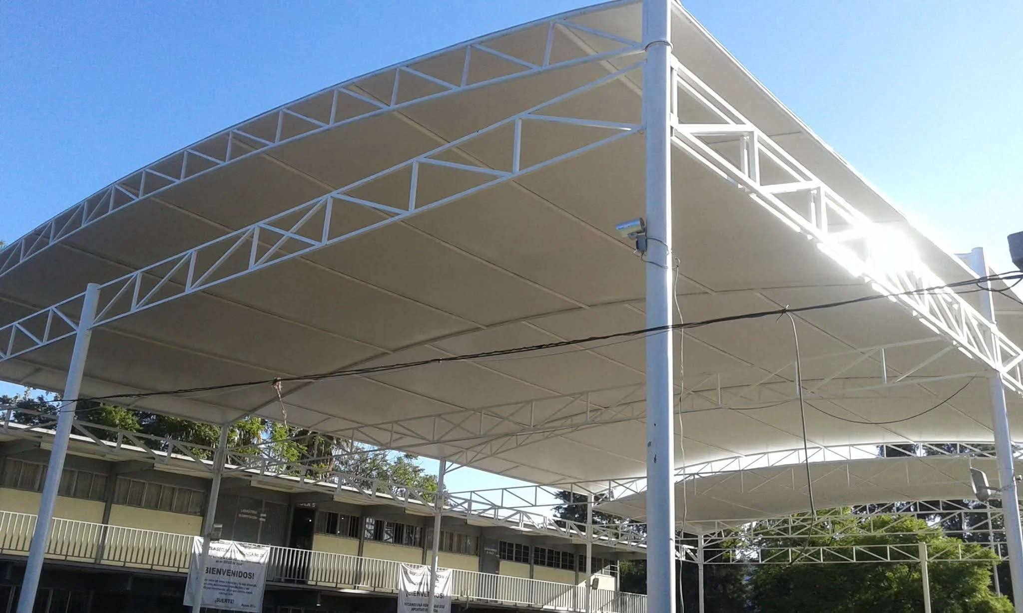 Estructura de columnas blancas con mallas blancas en un área abierta con fondos de edificios y árboles bajo cielo despejado.