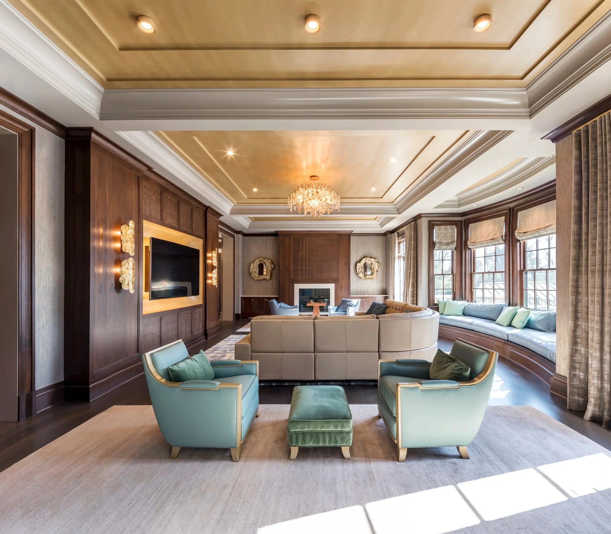 Elegant living room with large bay windows, beige and light green chairs, a cream sofa, a carpet, a chandelier, and wood-paneled walls.