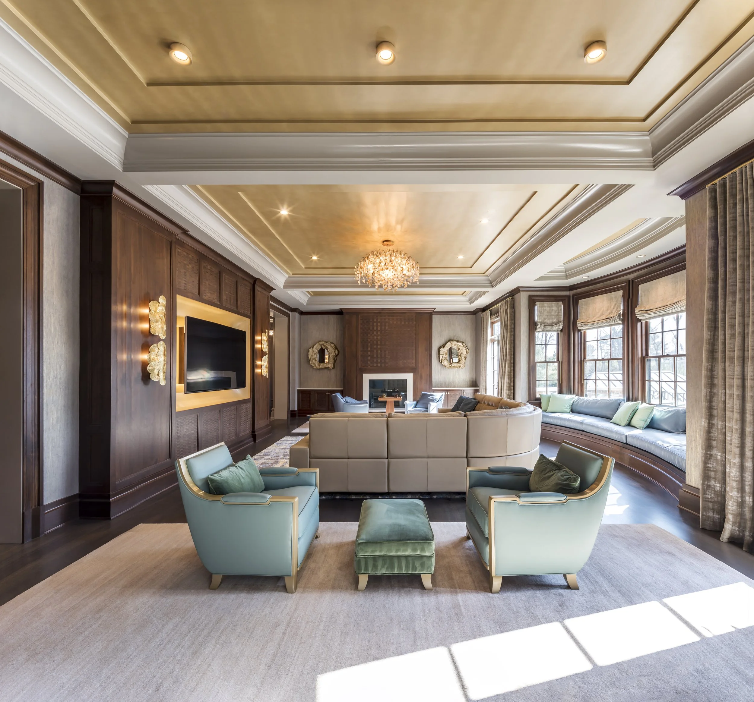 Elegant living room with large windows, a curved window seat with cushions, a central chandelier, a fireplace, and modern furniture.