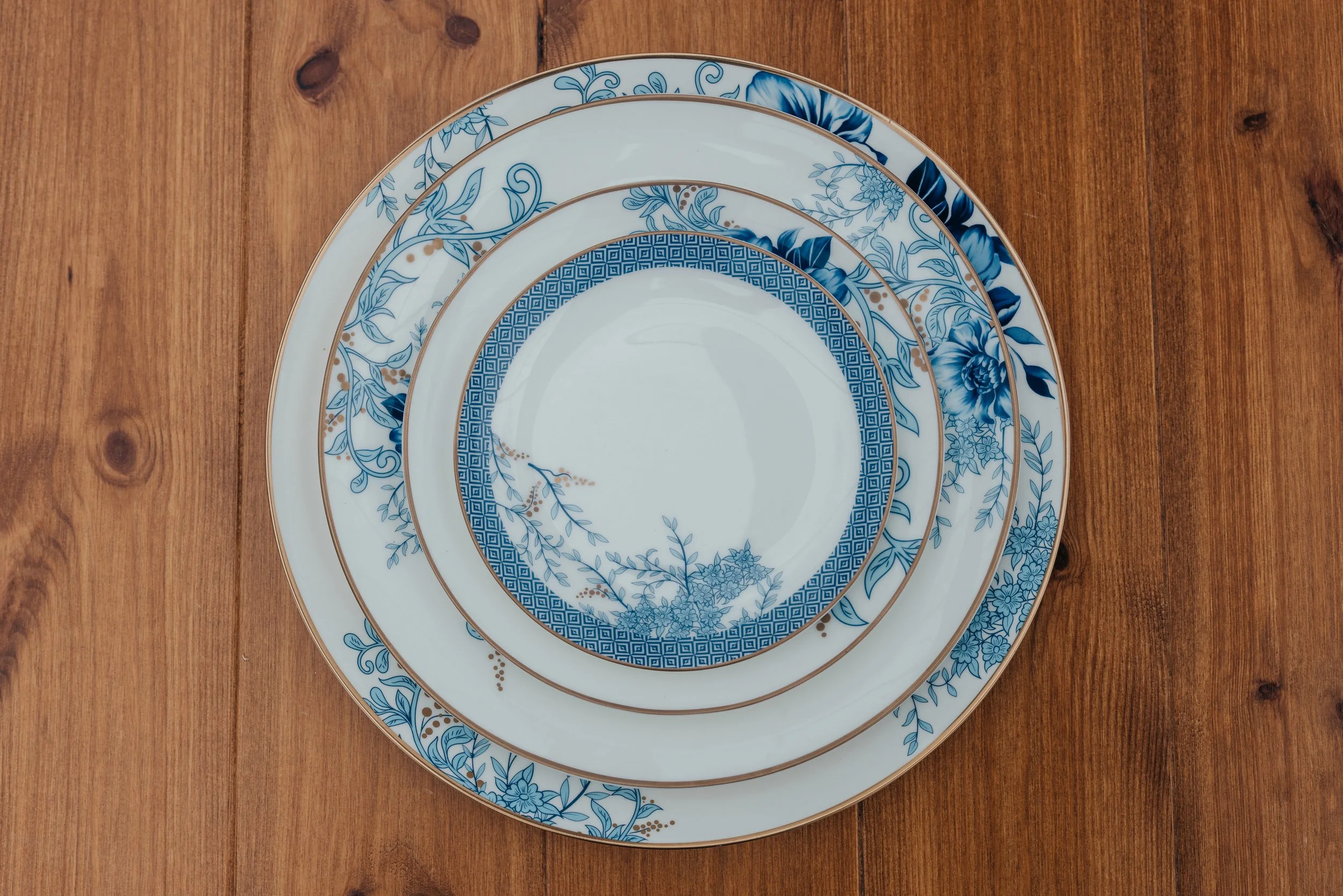 Stacked blue and white floral dinner plates with gold accents on a wooden table.