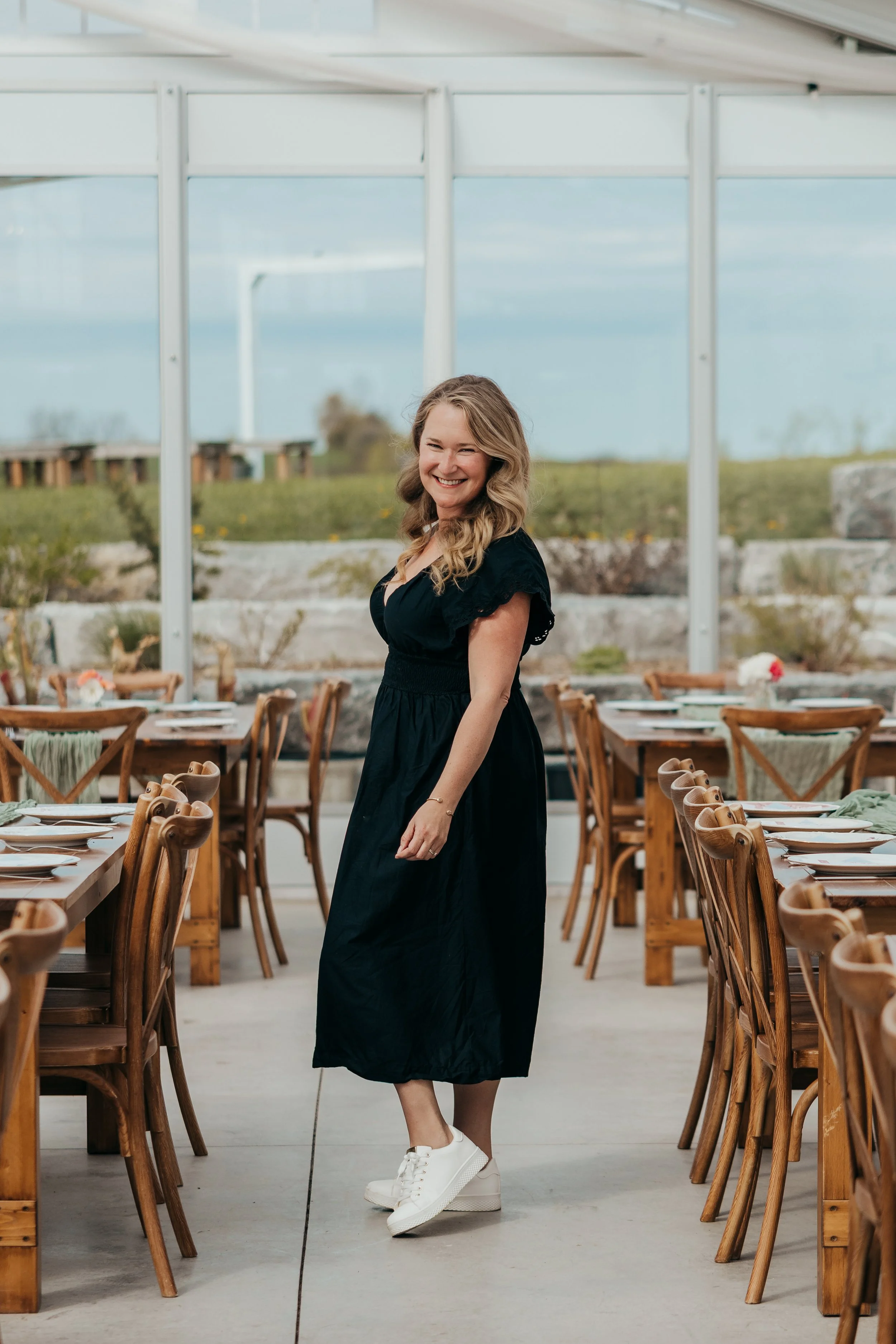 Owner and Lead Event Coordinator, Brittany is standing in a wedding venue wearing a black dress and smiling.