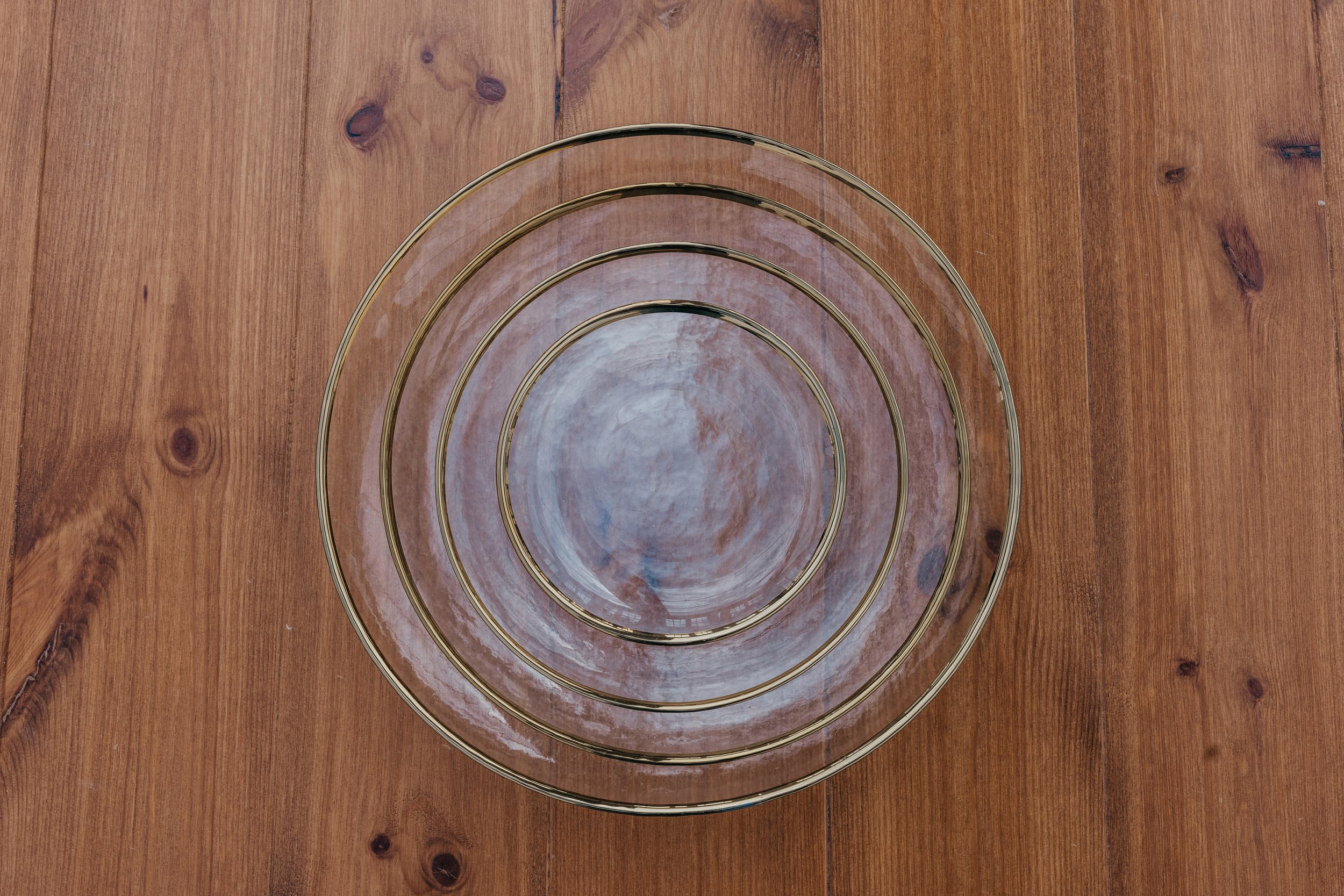 A set of four clear glass nesting bowls with gold-colored rims stacked inside each other on a wooden surface.