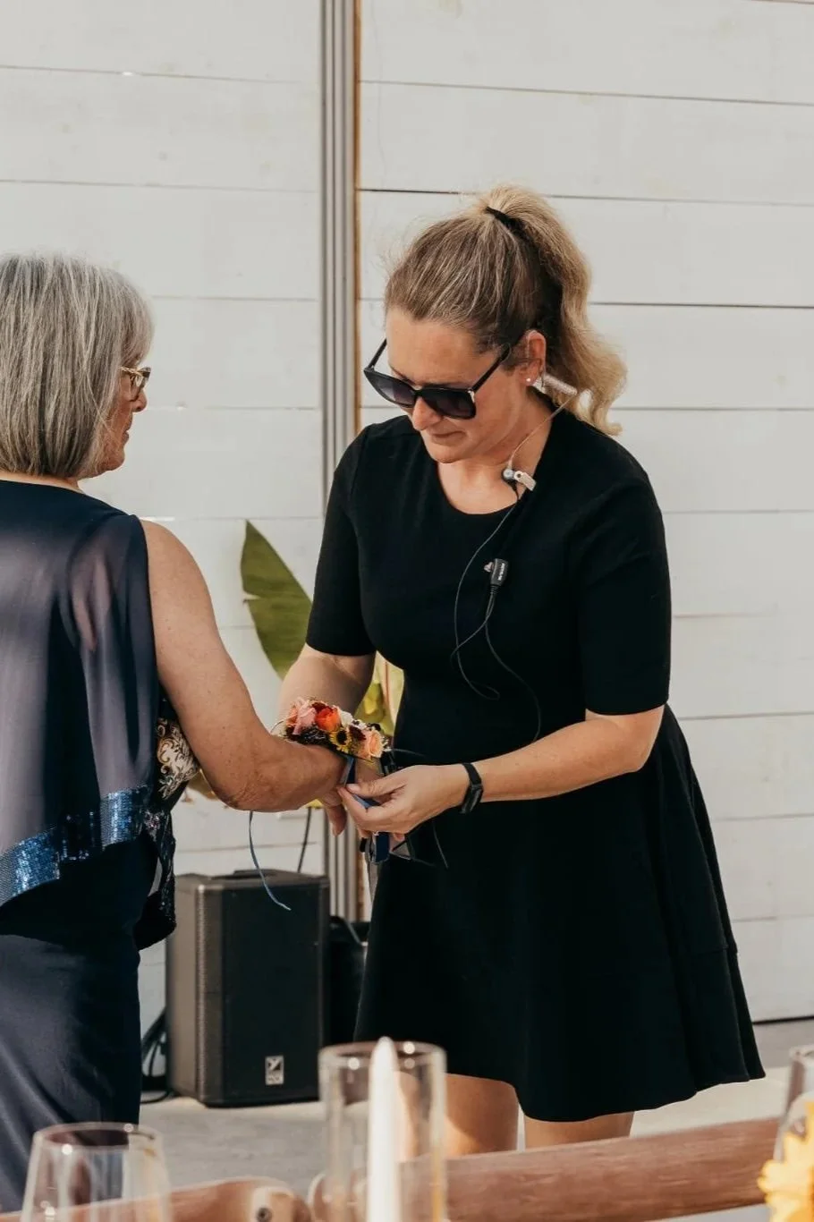 Brittany, Lead Event Coordinator is in black dress and is giving a small bouquet of flowers to another woman at an indoor event.