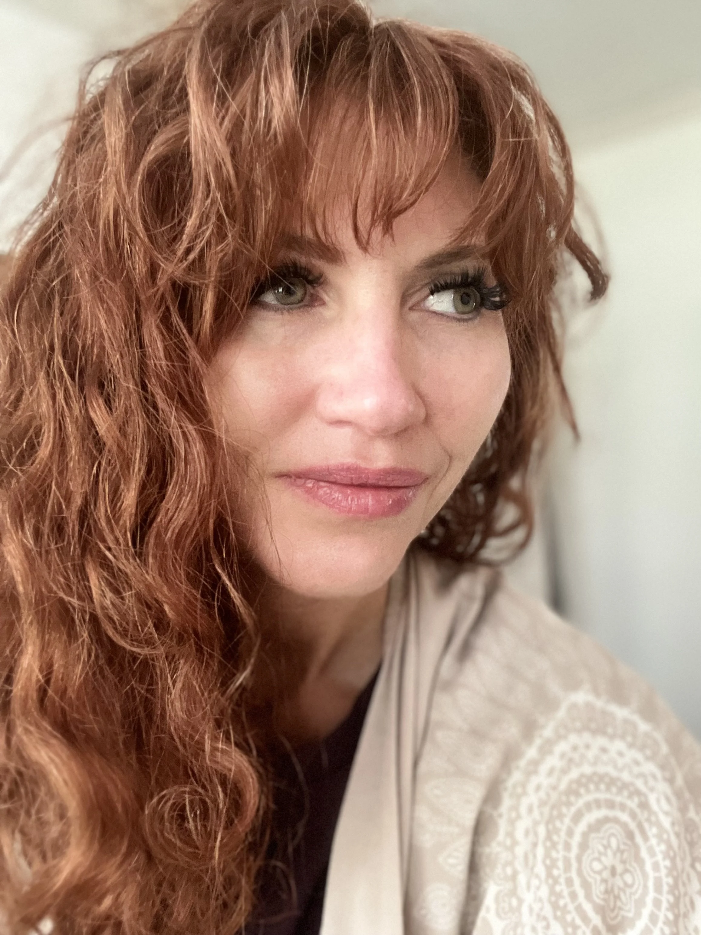 Close-up of a woman with curly red hair and green eyes looking to the side.
