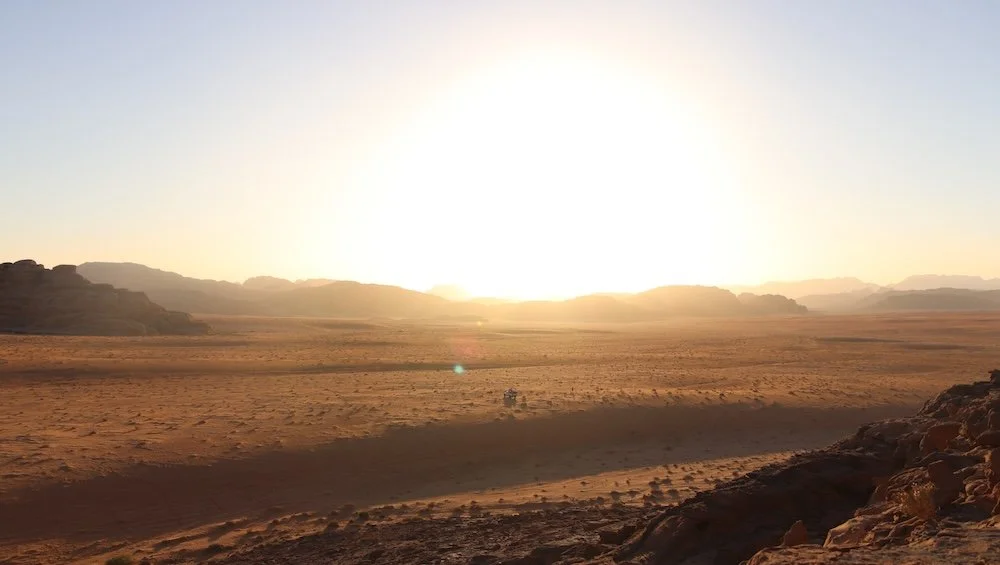 Paysage désertique immense, aux couleurs chaudes. Un 4x4 au milieu au loin. 